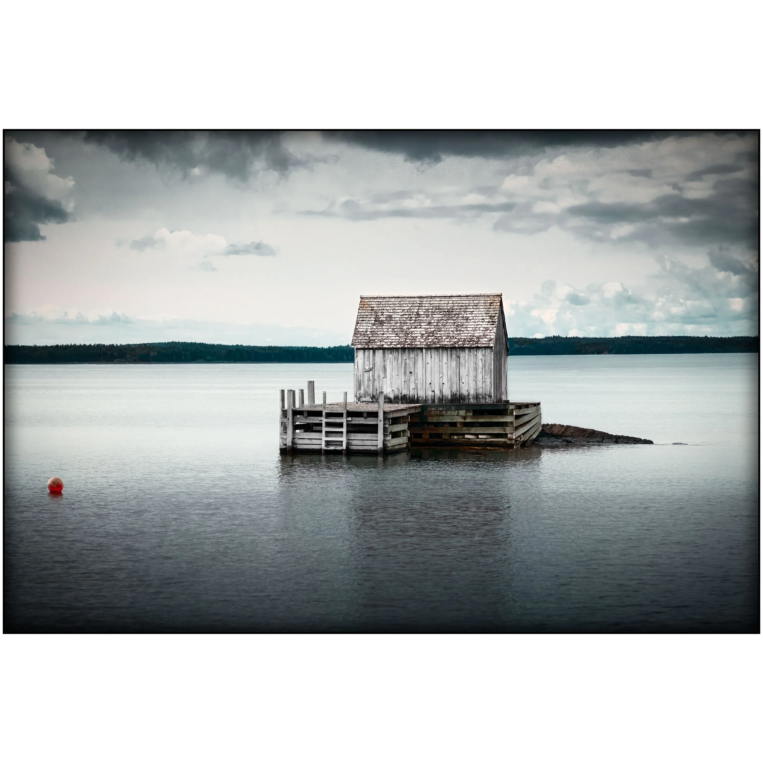 A grey wooden fishing hut sits on a small dock surrounded by still water, with a distant shoreline and heavy clouds in the background.