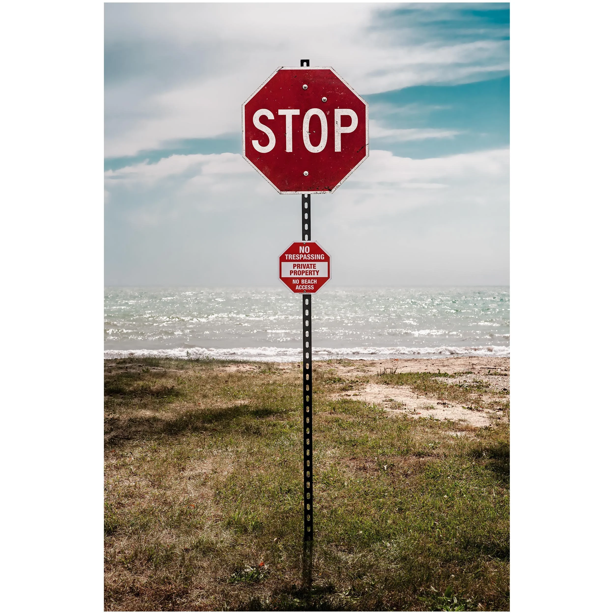 A red stop sign with additional warning signs below it, placed near the beach with ocean waves and a cloudy sky in the background.