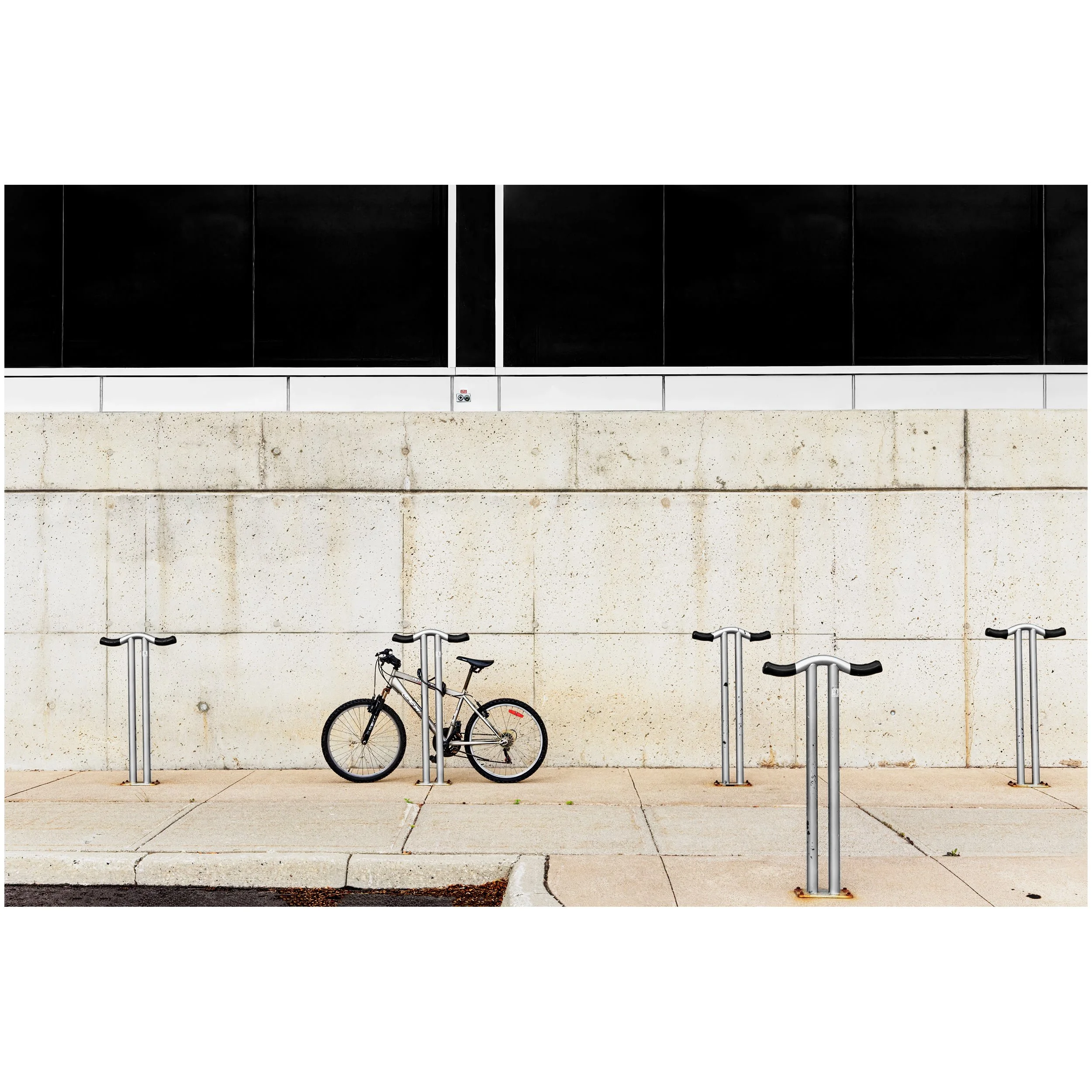 Bicycle parked at a bike rack in front of a modern building with black panels and a concrete base.