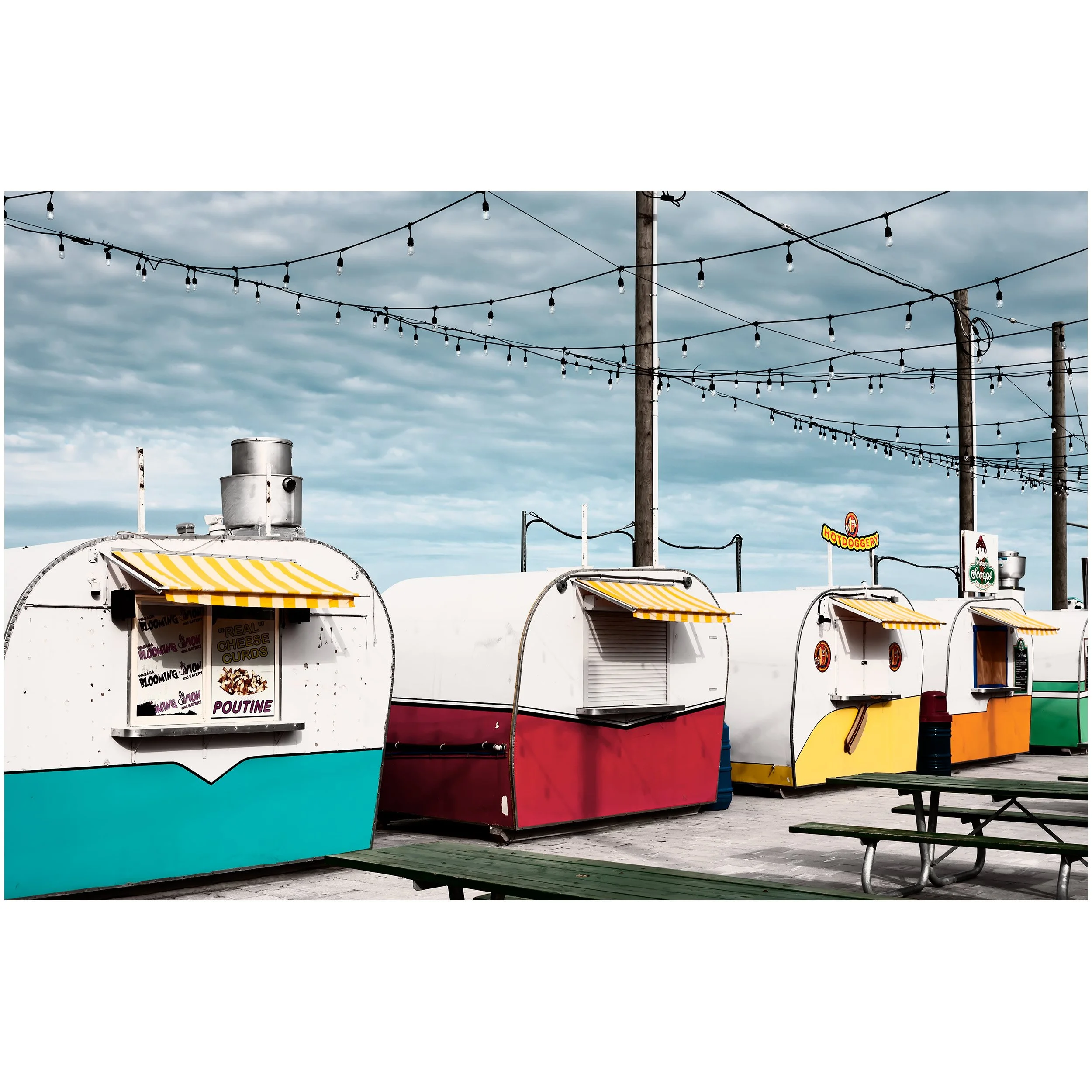 Outdoor food market stalls with striped awnings and string lights overhead on cloudy day.