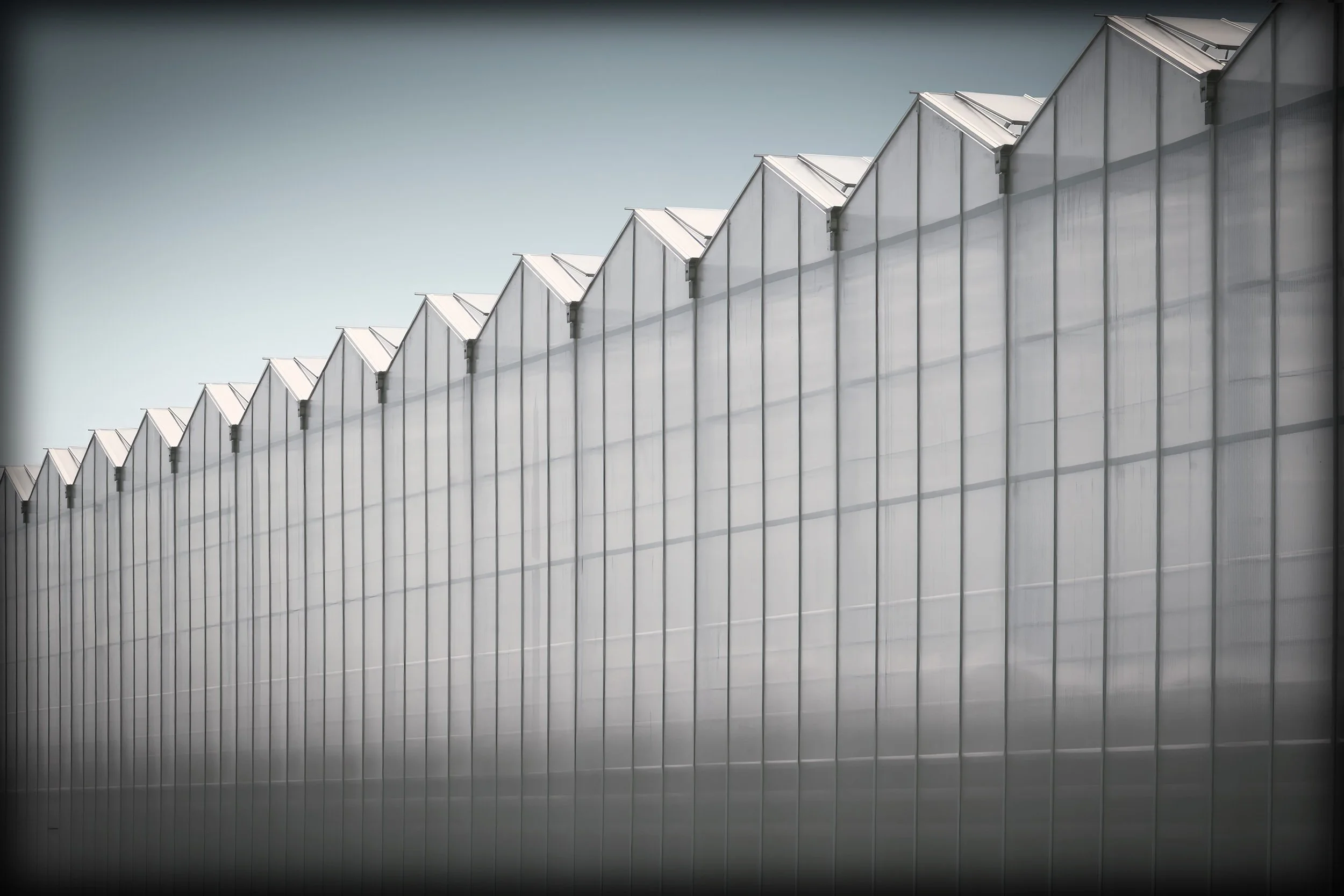 Exterior view of a large industrial building with a sharply peaked roof, made of metallic panels under a clear sky.