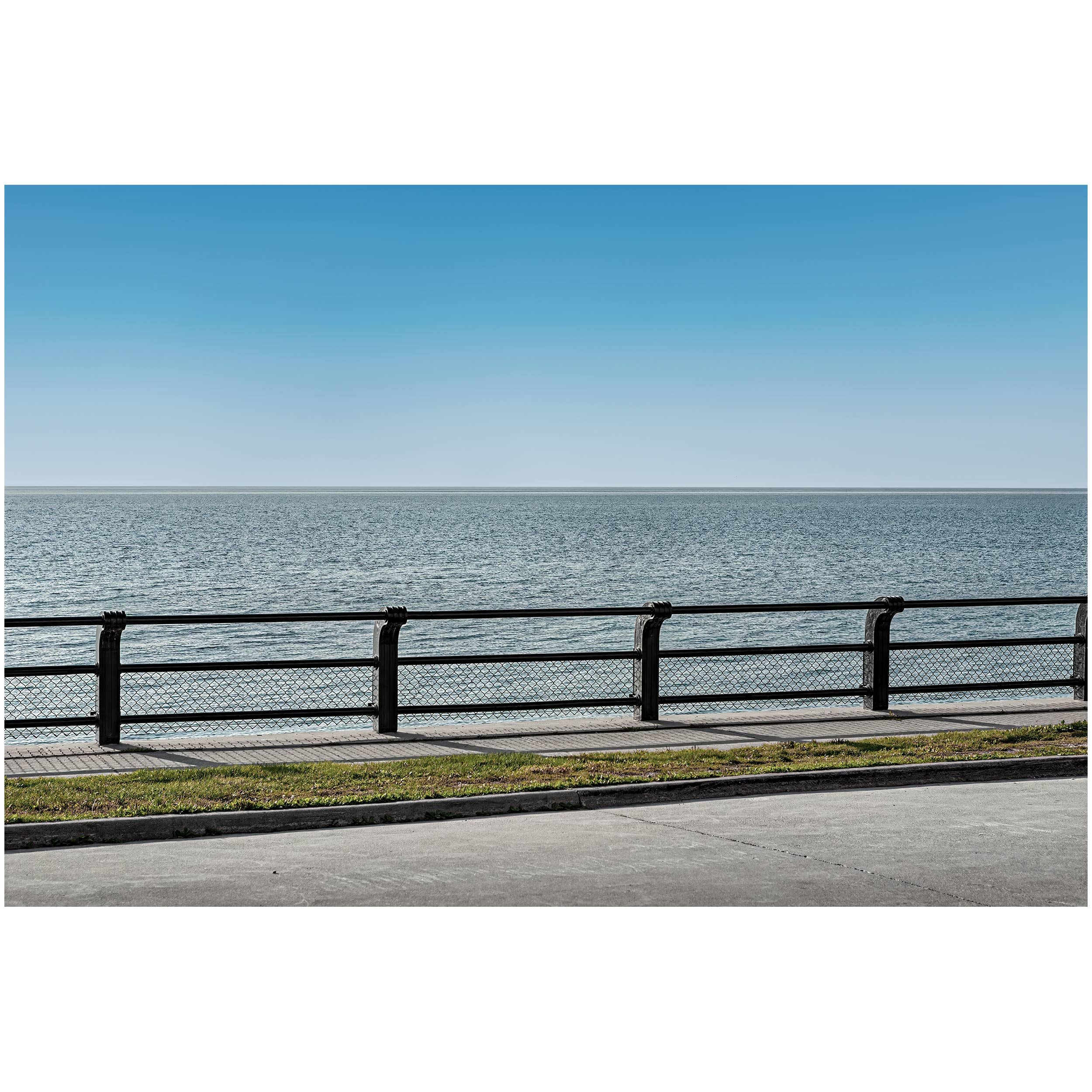 View of a calm lake Ontario with a barrier and a fence in the foreground, under a clear blue sky.