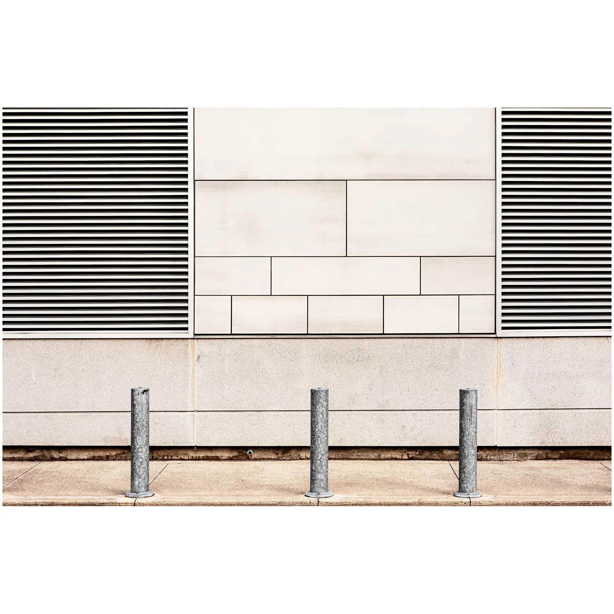 A section of a beige building with metal vents and three metal bollards in front of it.