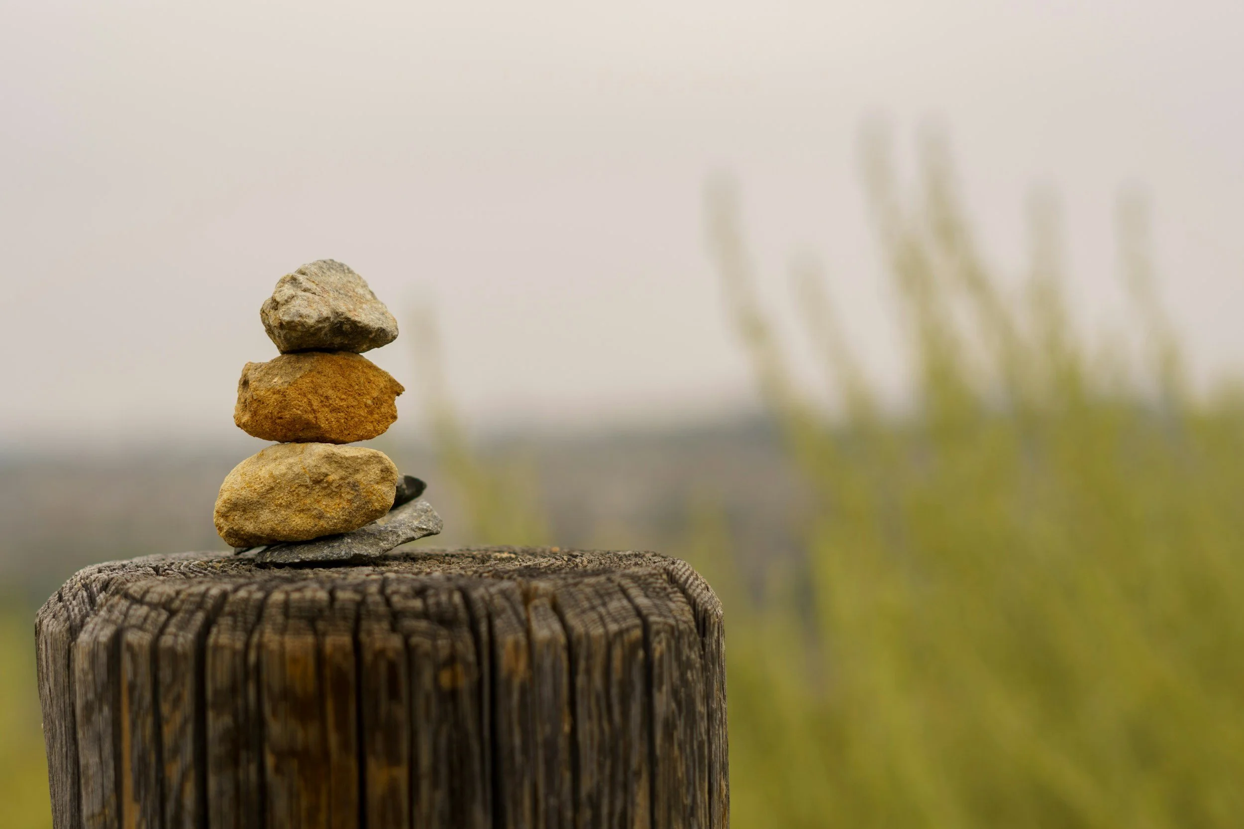 Stacked rocks on a weathered wooden post outdoors, with blurred greenish background.