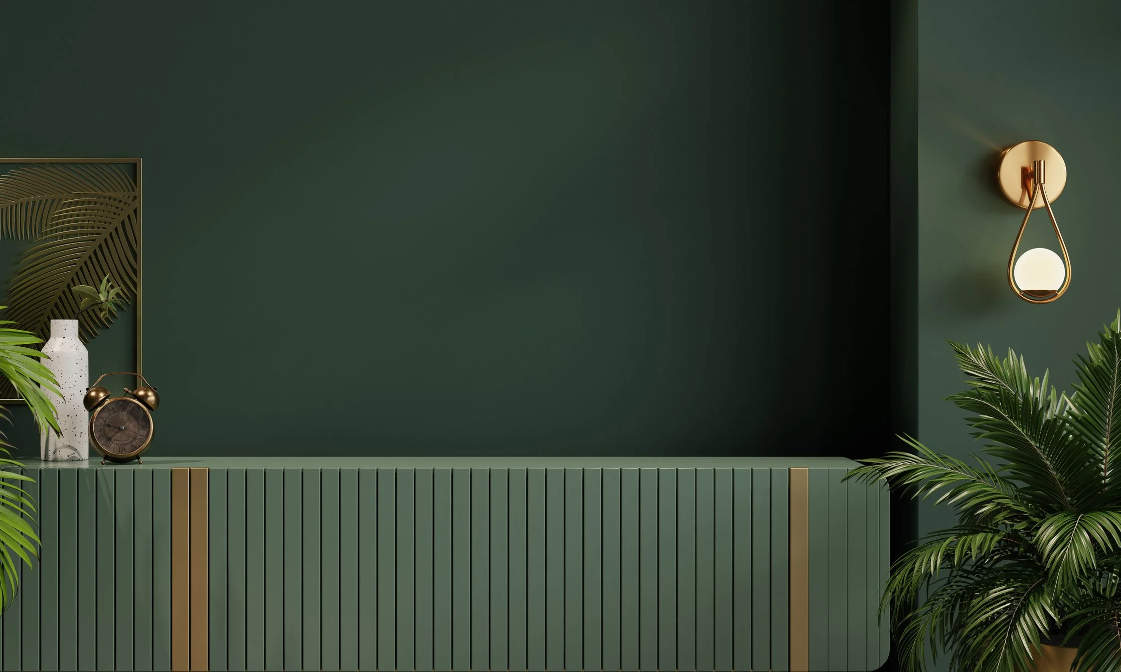 Decorative wall with a green background, a gold wall lamp with a white spherical bulb, a white speckled vase, an old-fashioned alarm clock, green plants, and a framed poster with palm leaves.