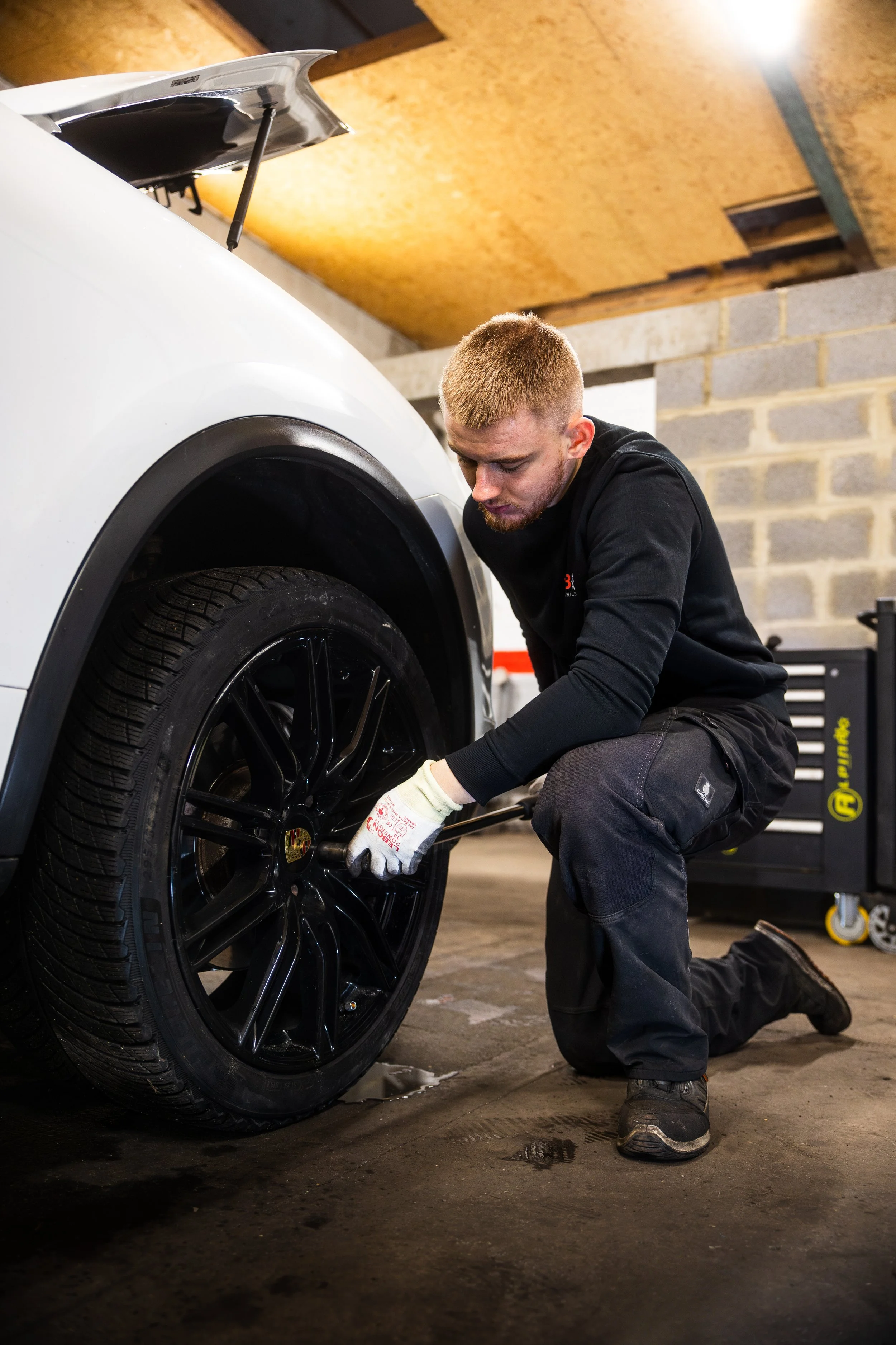 Un homme en train de changer un pneu de voiture dans un atelier mécanique à Verviers.