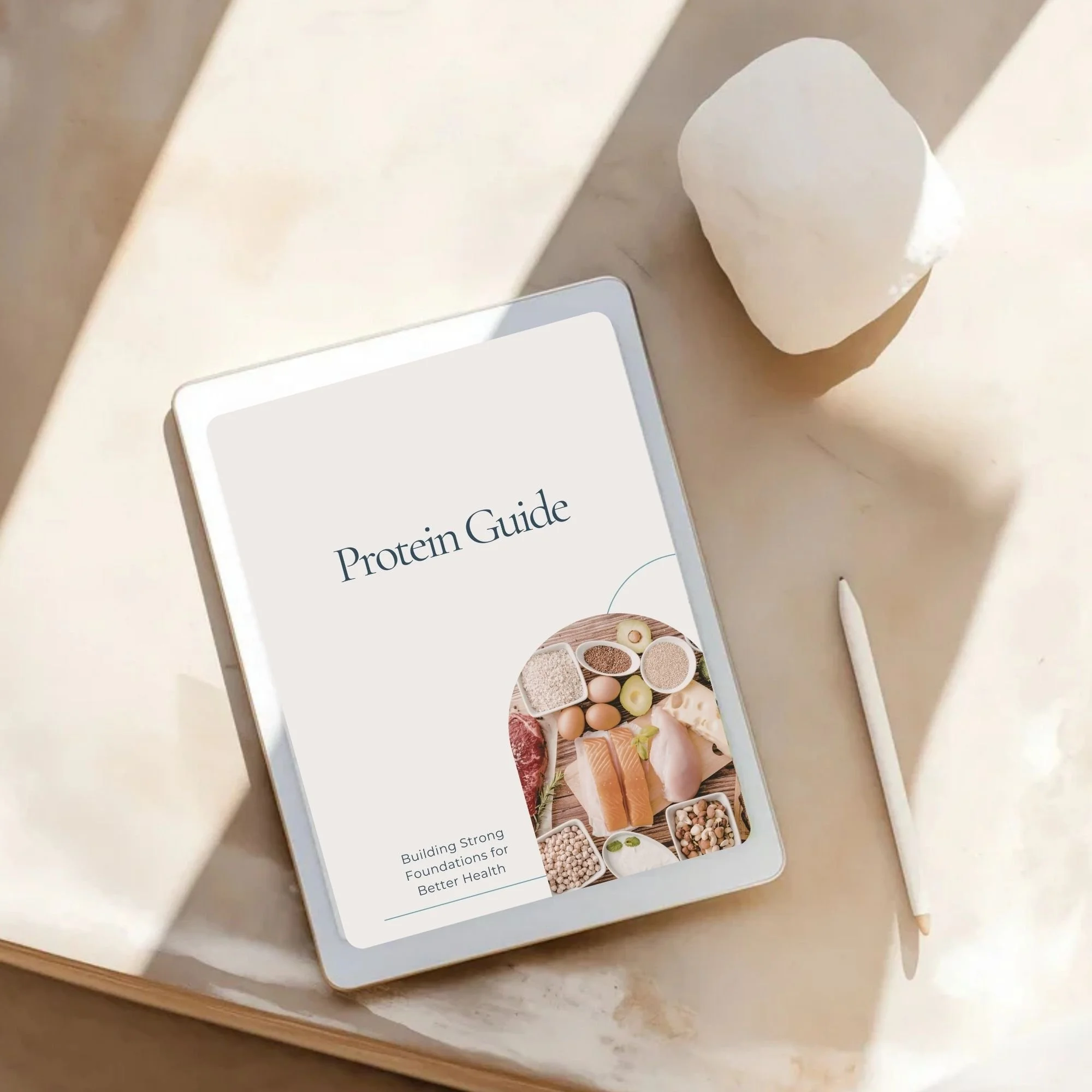 Digital tablet displaying a 'Protein Guide' cover with an image of various protein foods, placed on a light-colored marble surface beside a white stylus and a piece of white chalk.