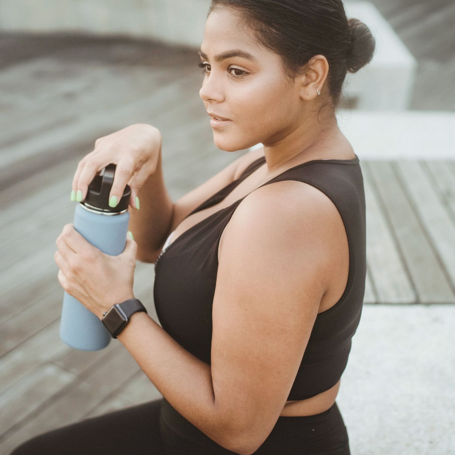 A woman in a black sports bra holding a blue water bottle.