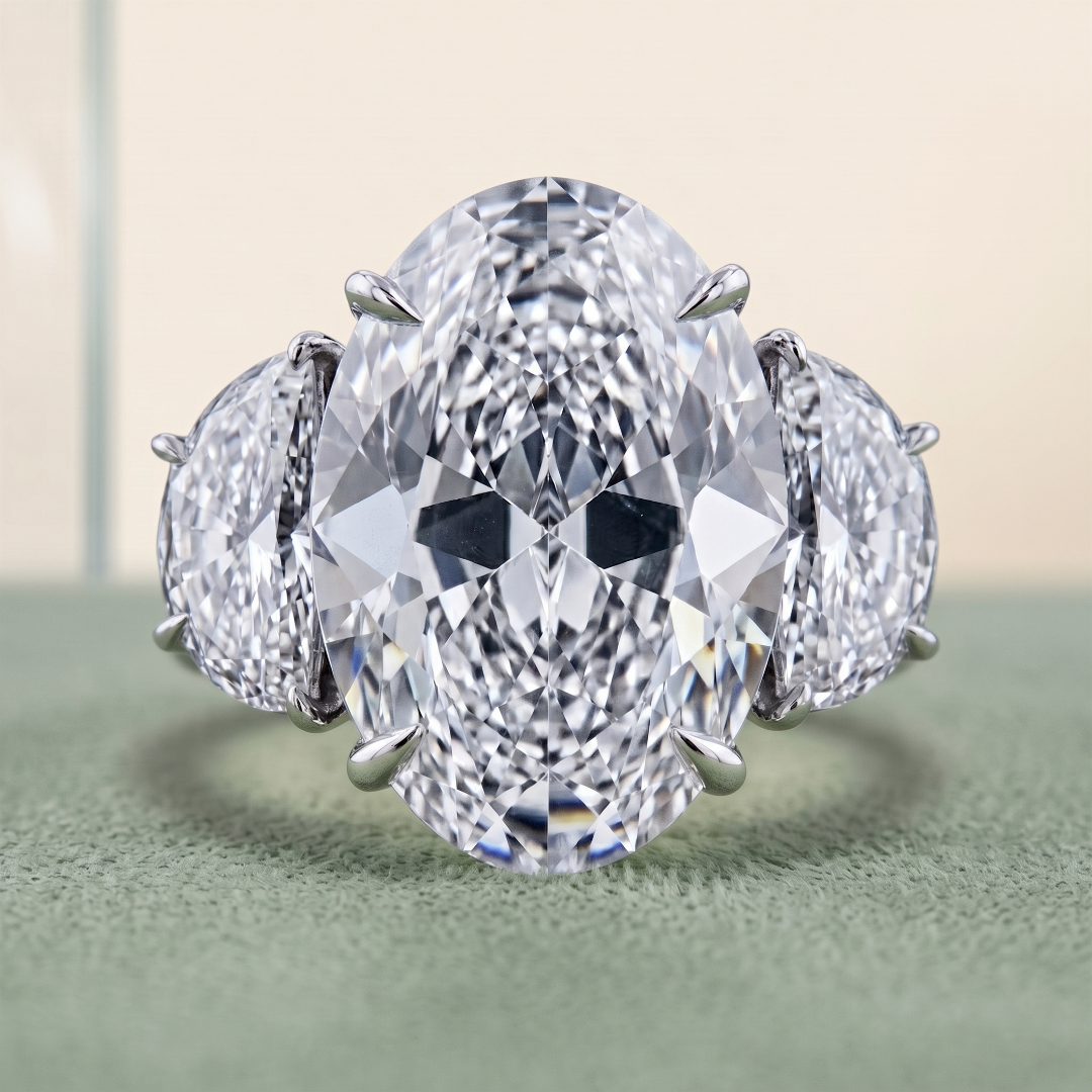 Close-up of a large, oval-cut diamond ring with smaller diamonds on the band, set in a silver or white gold setting, displayed on a textured green surface.