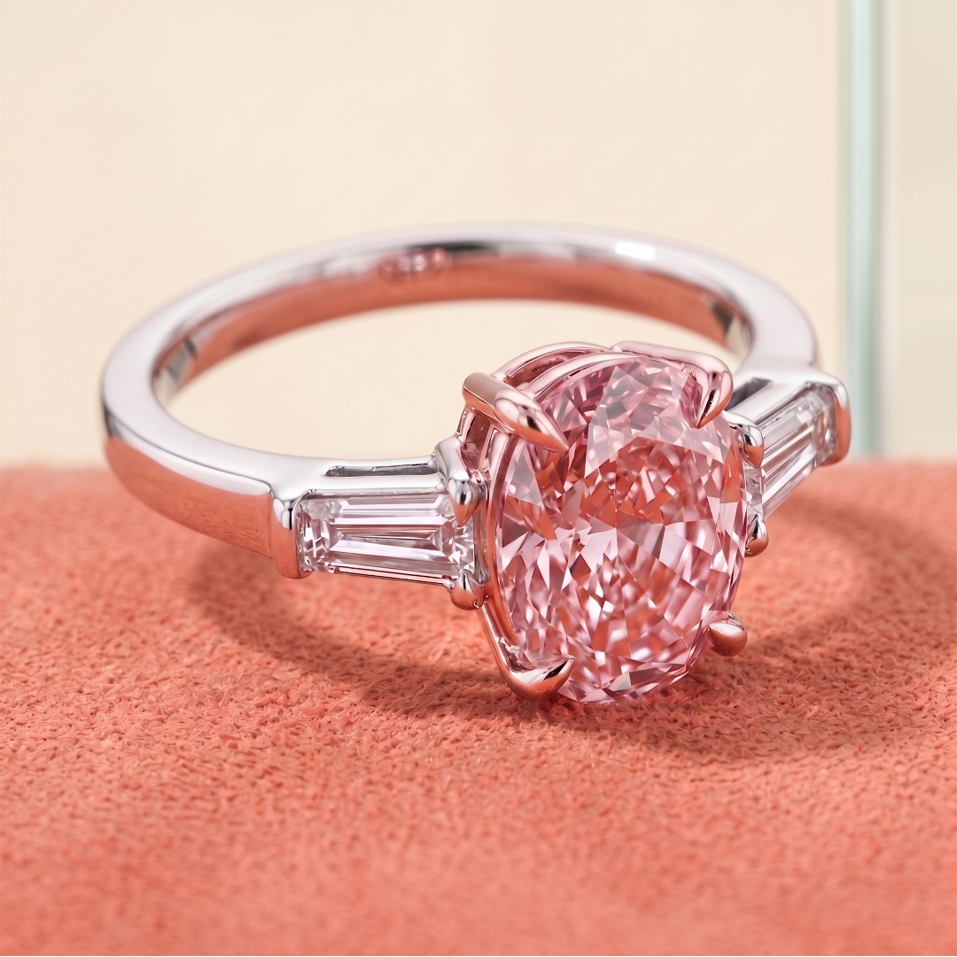 A silver ring with a large pink oval-shaped gemstone and baguette-cut diamonds on each side, resting on a pink textured surface.