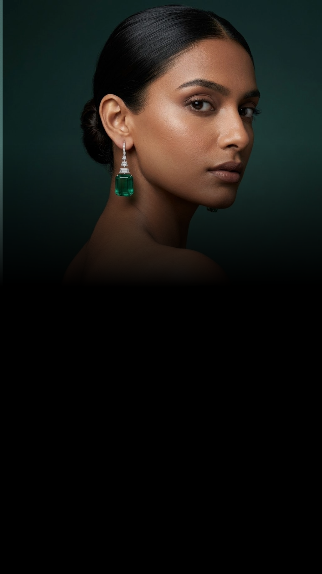 A woman with dark hair styled in a bun, wearing large emerald green earrings and makeup, looking at the camera with a neutral expression against a dark green background.