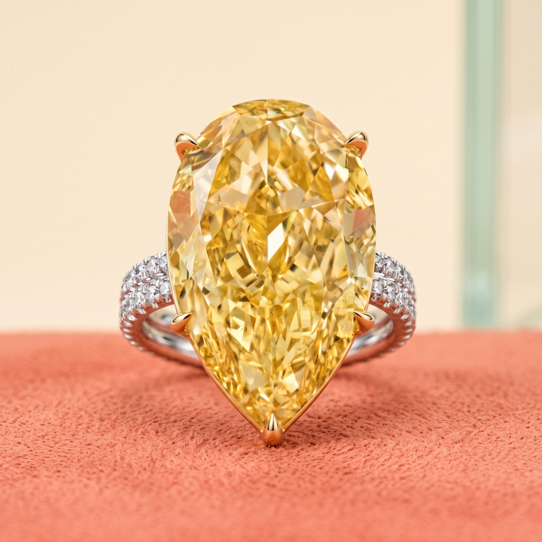 A large marquise-cut yellow diamond ring with a diamond-studded band on a textured pink surface.