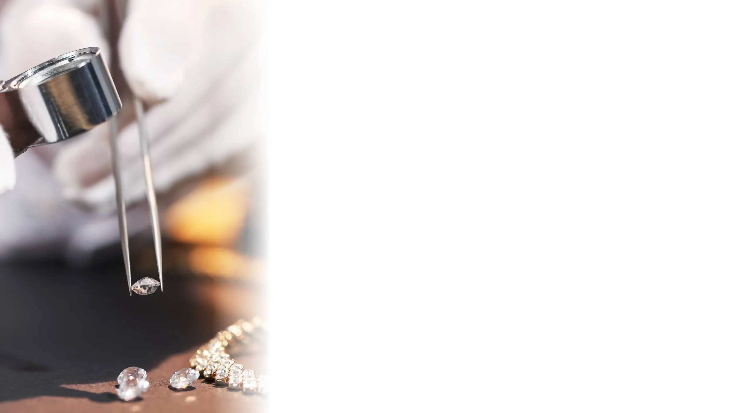 Close-up of a jeweler's hand holding tweezers with a diamond, with other diamonds and jewelry pieces on a black surface.