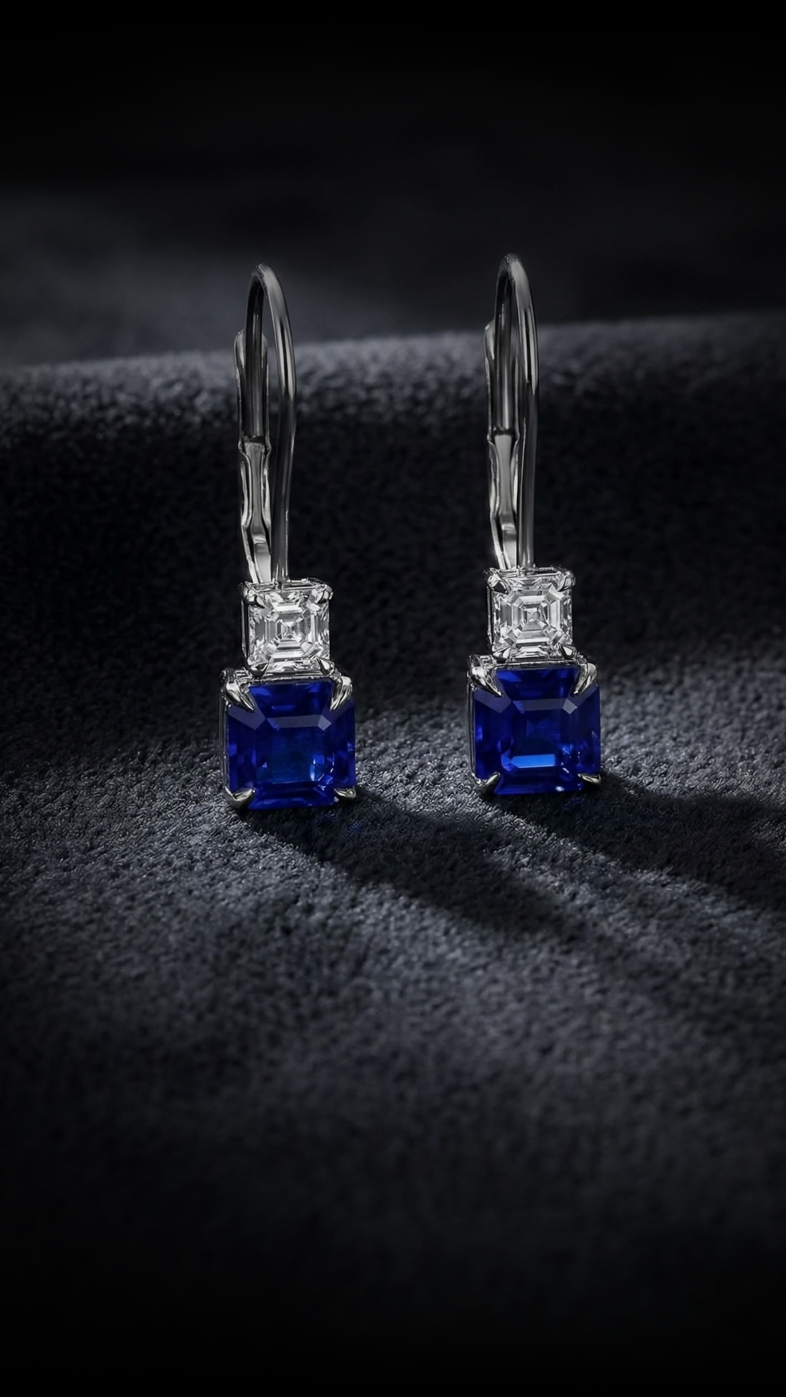 Pair of silver earrings with blue and clear gemstones on a black textured fabric.