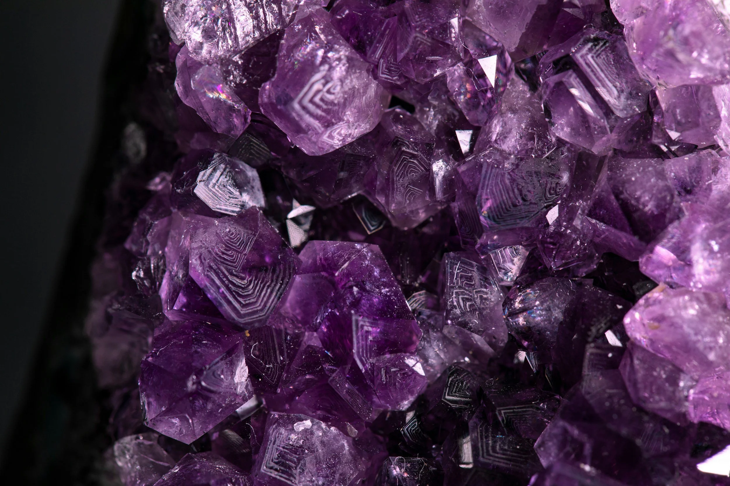 Close-up view of a cluster of purple amethyst crystals showing geometric growth patterns and reflective surfaces.