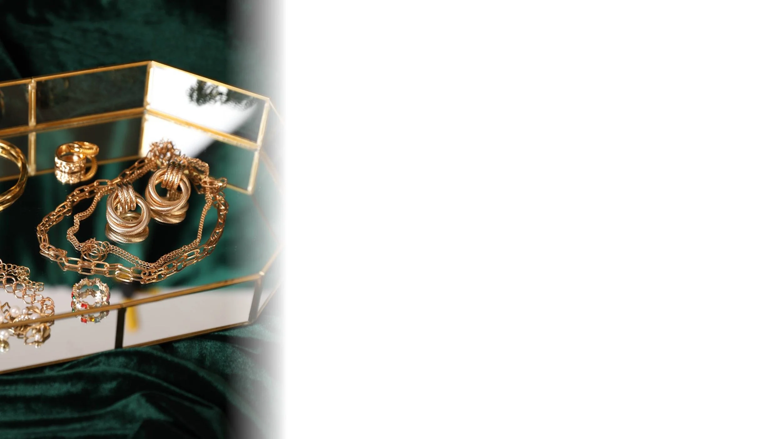 Gold jewelry, including rings, necklaces, and earrings, displayed on a green velvet surface inside a decorative glass box with a gold frame.