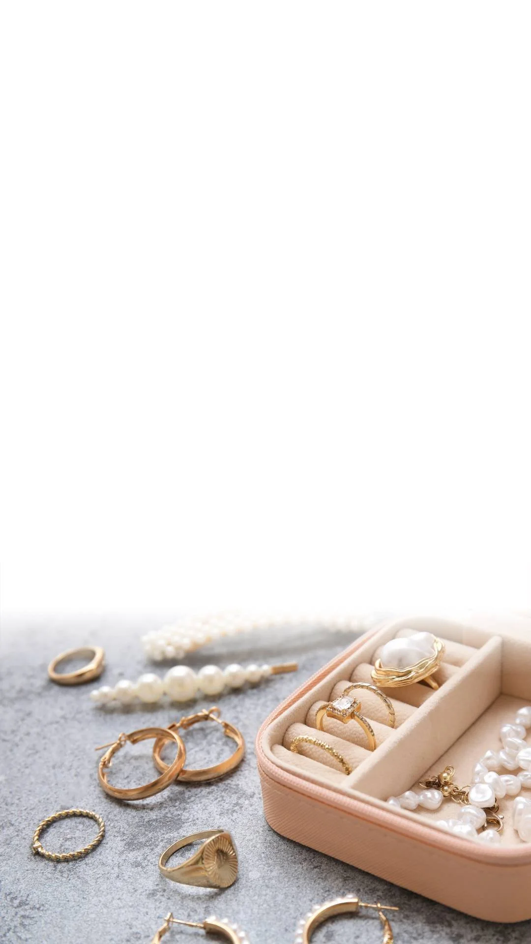 Jewelry collection with gold rings, pearl necklaces, and earrings on a gray surface, with an open jewelry box in the corner.