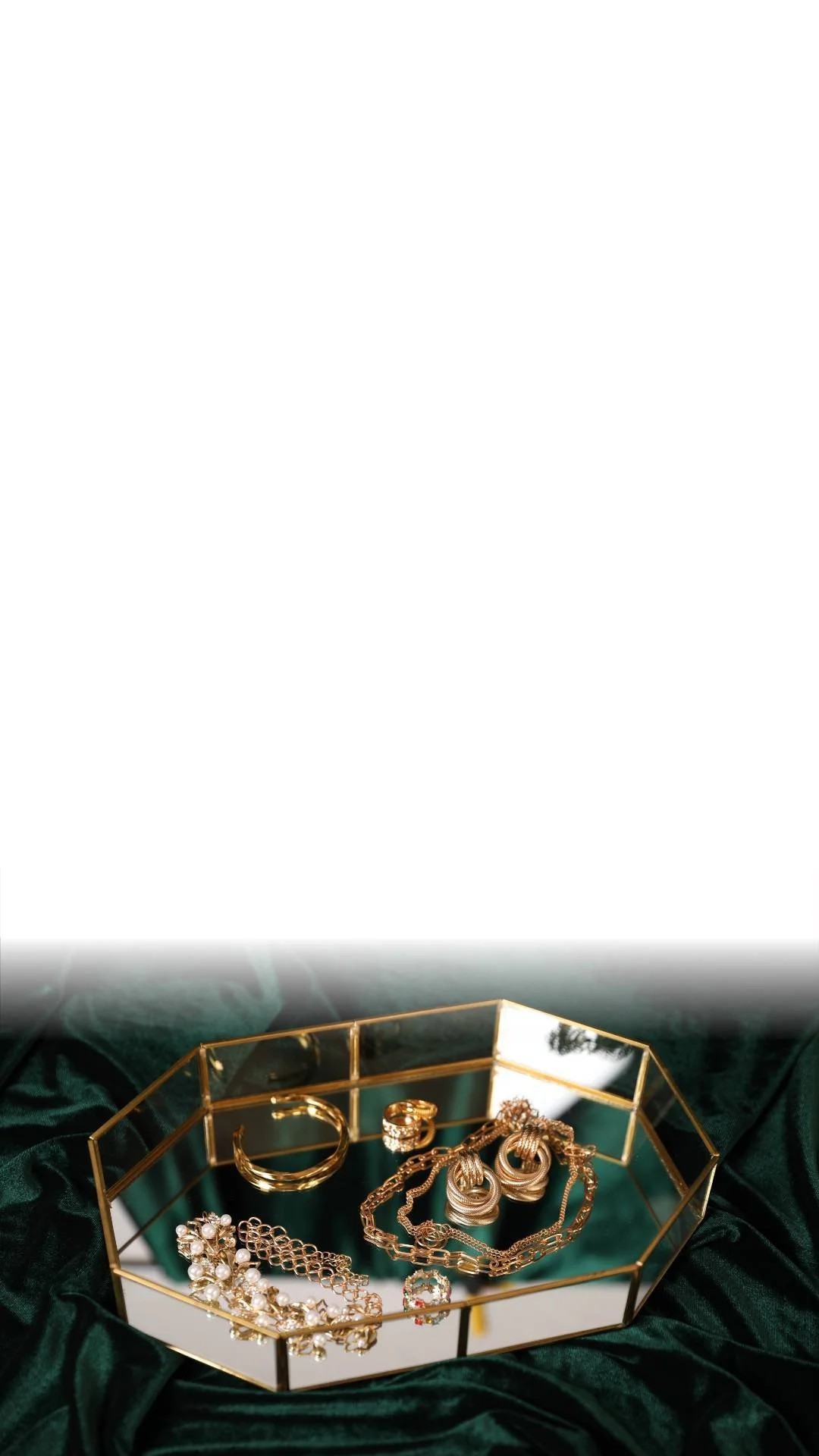 Gold jewelry, including rings, necklaces, bracelets, and earrings, displayed on a mirrored tray with dark green velvet fabric background.