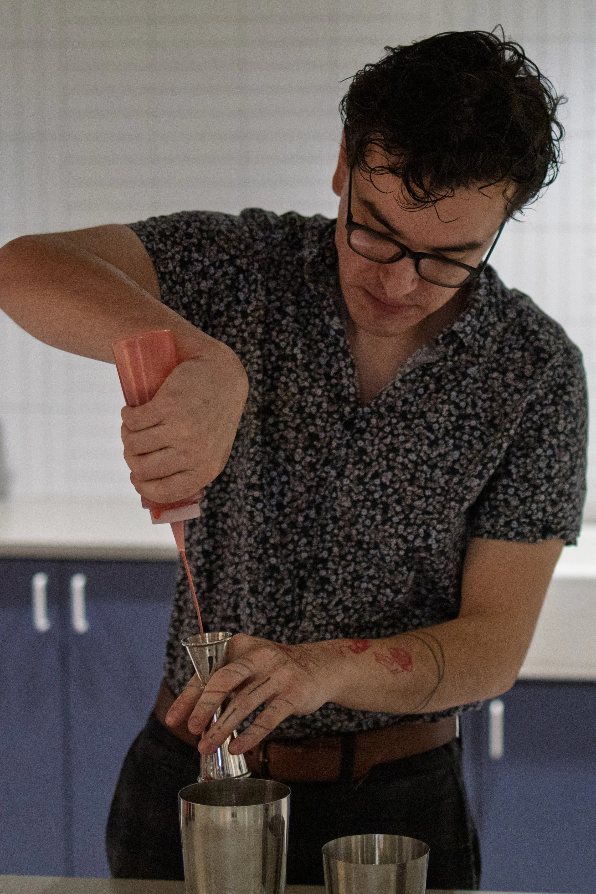 Person pouring pink liquid from squeeze bottle into a jigger in a kitchen.