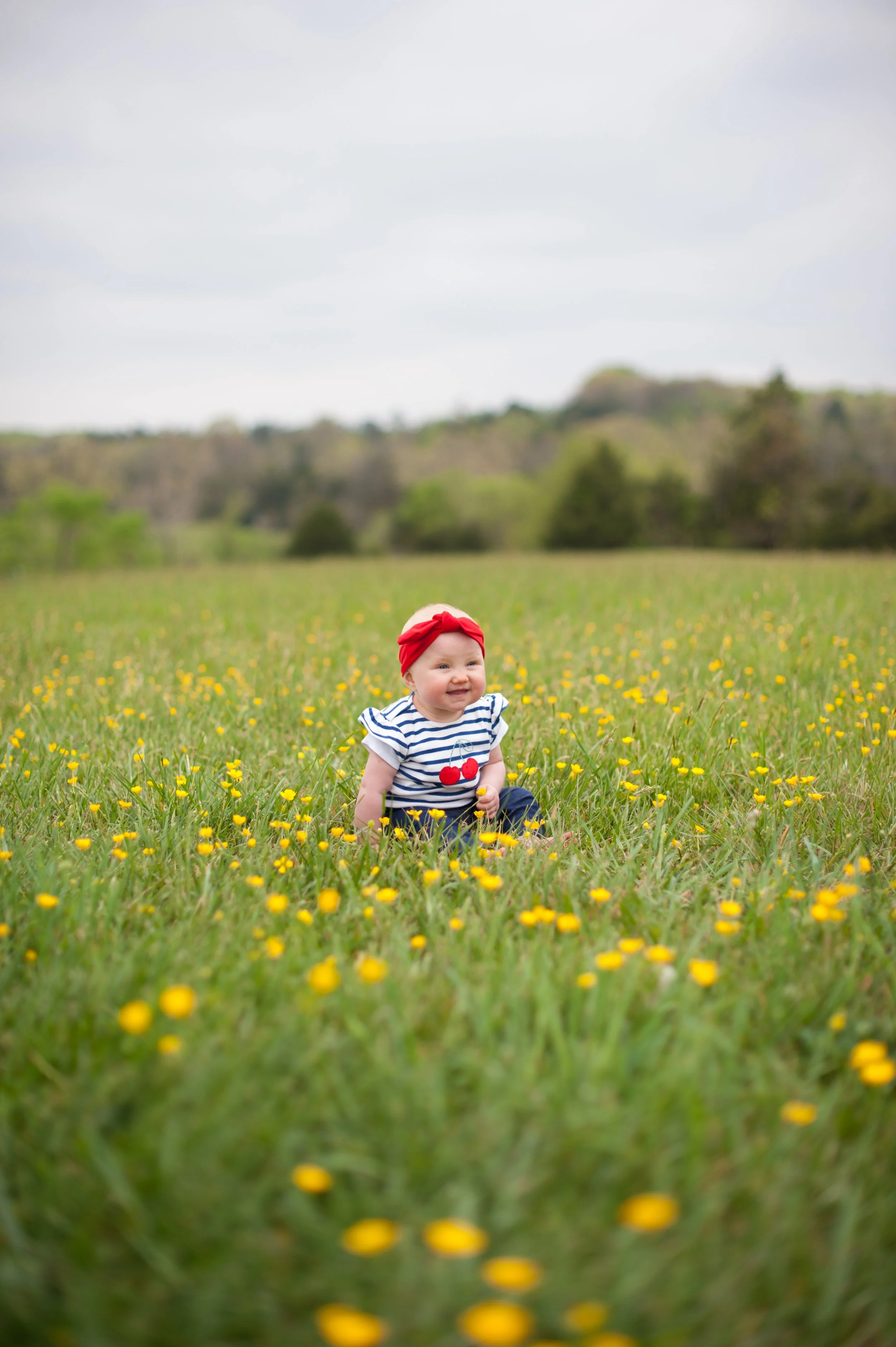 Child in a red headband and striped shirt sitting in a yellow flower field.