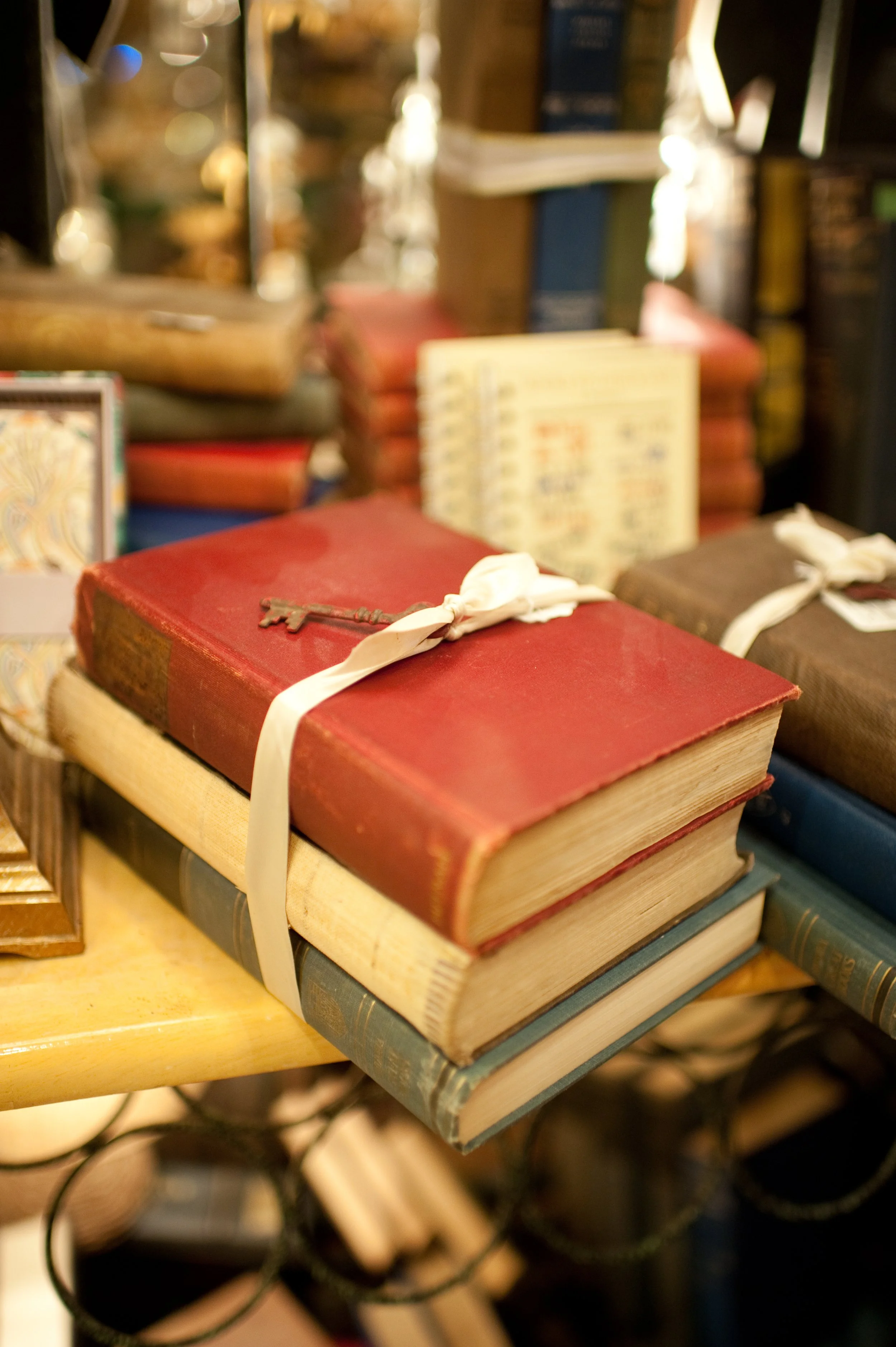 Close-up of a pile of vintage books tied together with a white ribbon, with an old key placed on top, displayed on a wooden table.