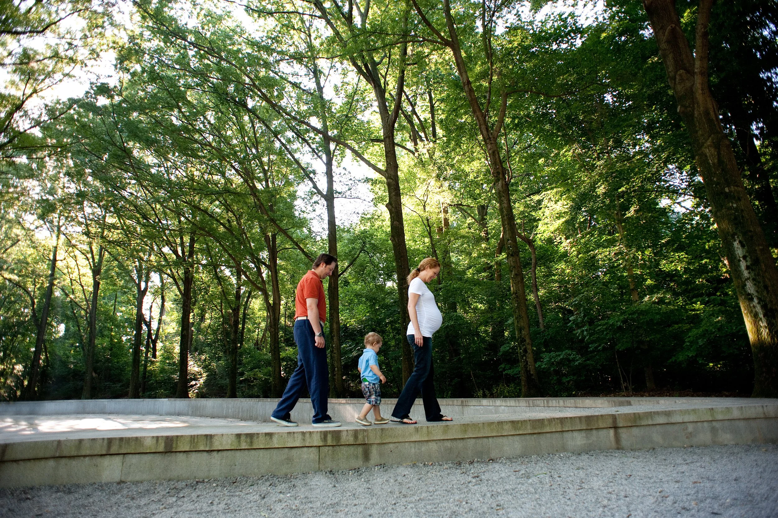 Family with pregnant woman, man, and two children walking on a stone path in a lush green forest.