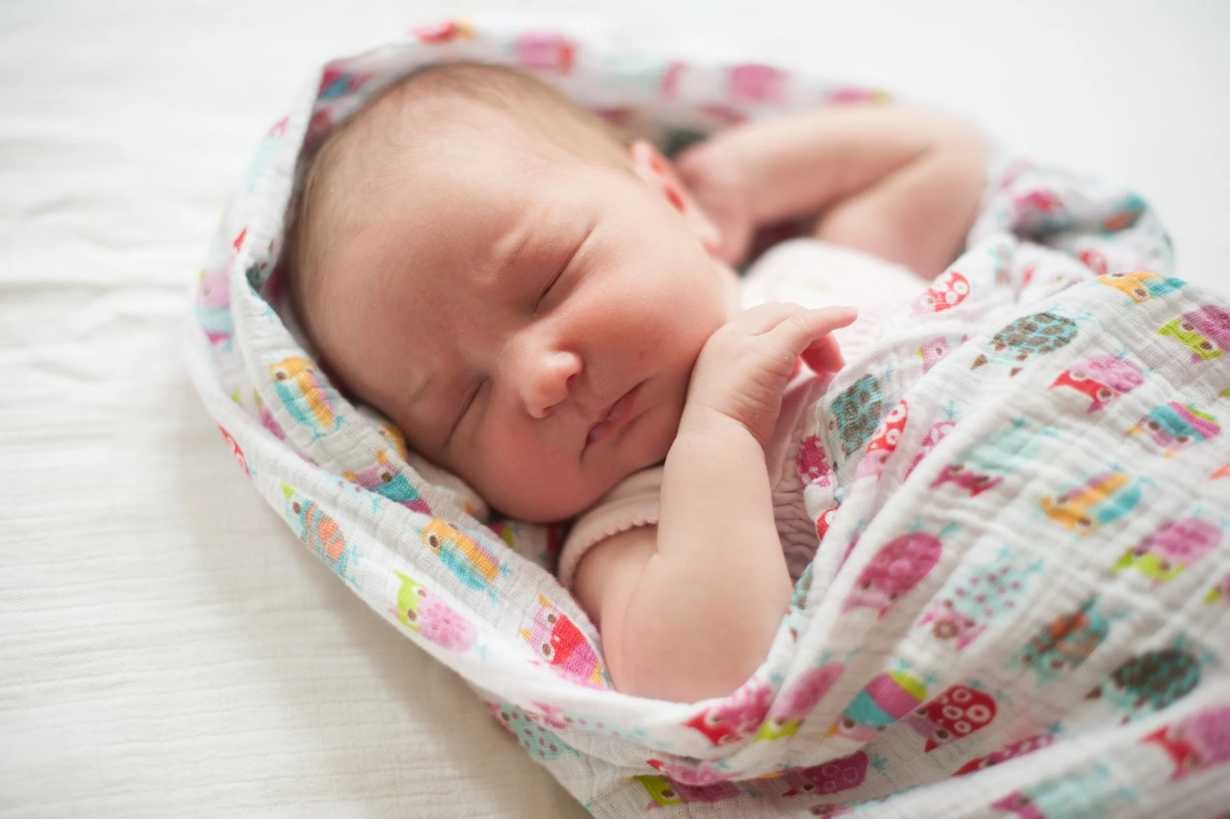 A sleeping newborn baby wrapped in a colorful, patterned blanket with closed eyes and a relaxed facial expression.