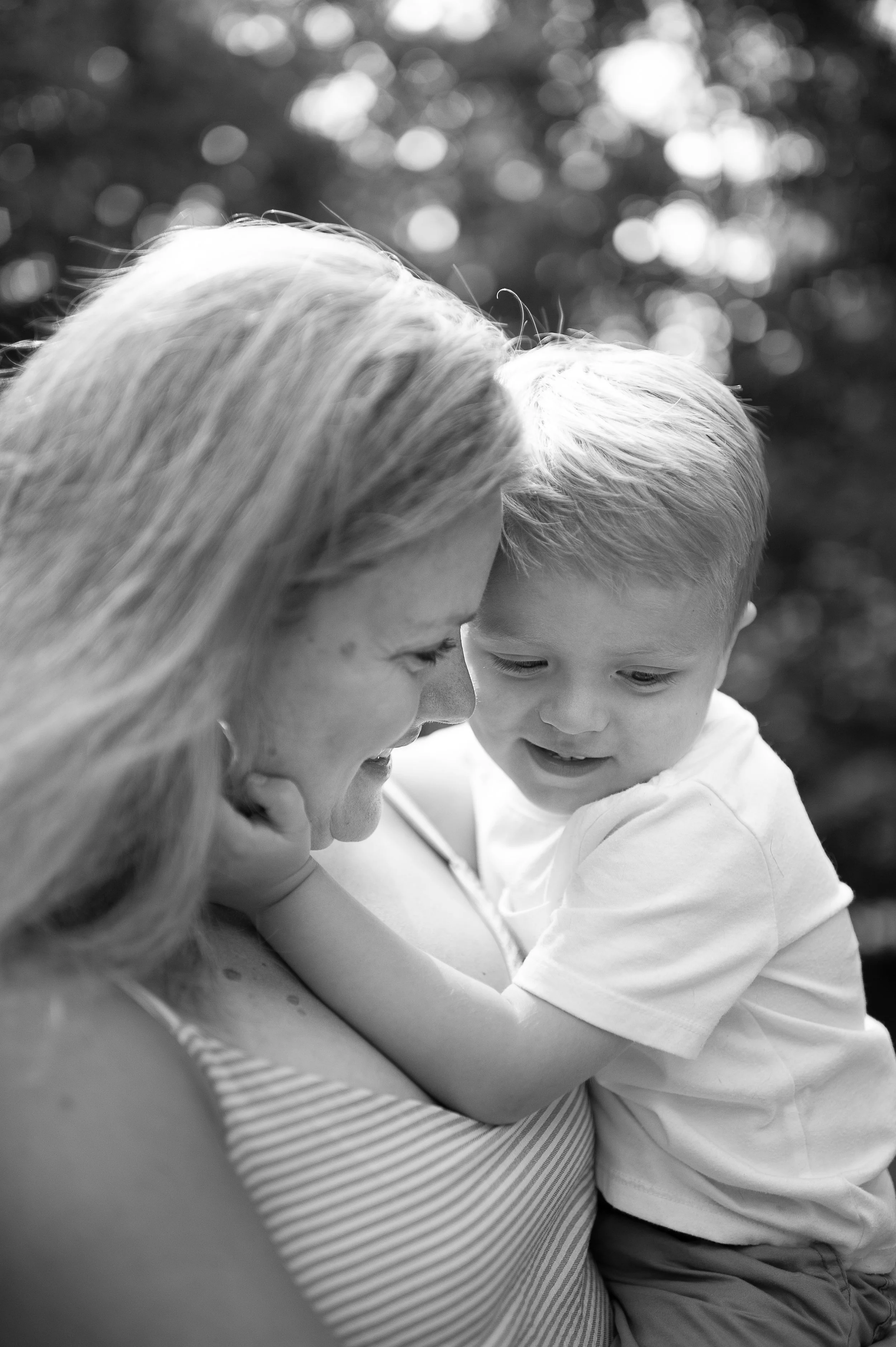A black and white photograph of a woman and a young boy close together, sharing a tender moment outdoors.