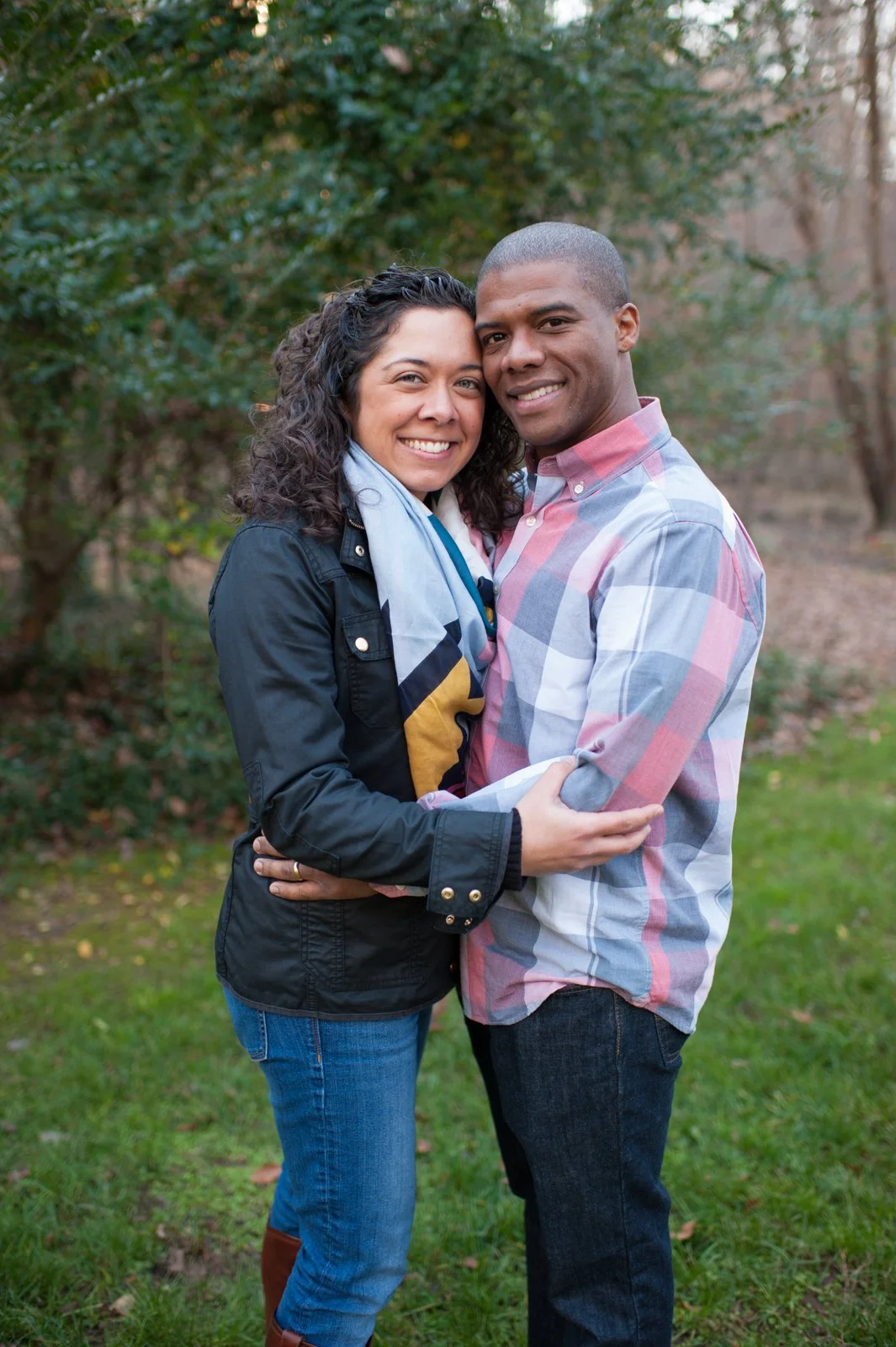 A smiling couple embracing outdoors, surrounded by trees and grass.
