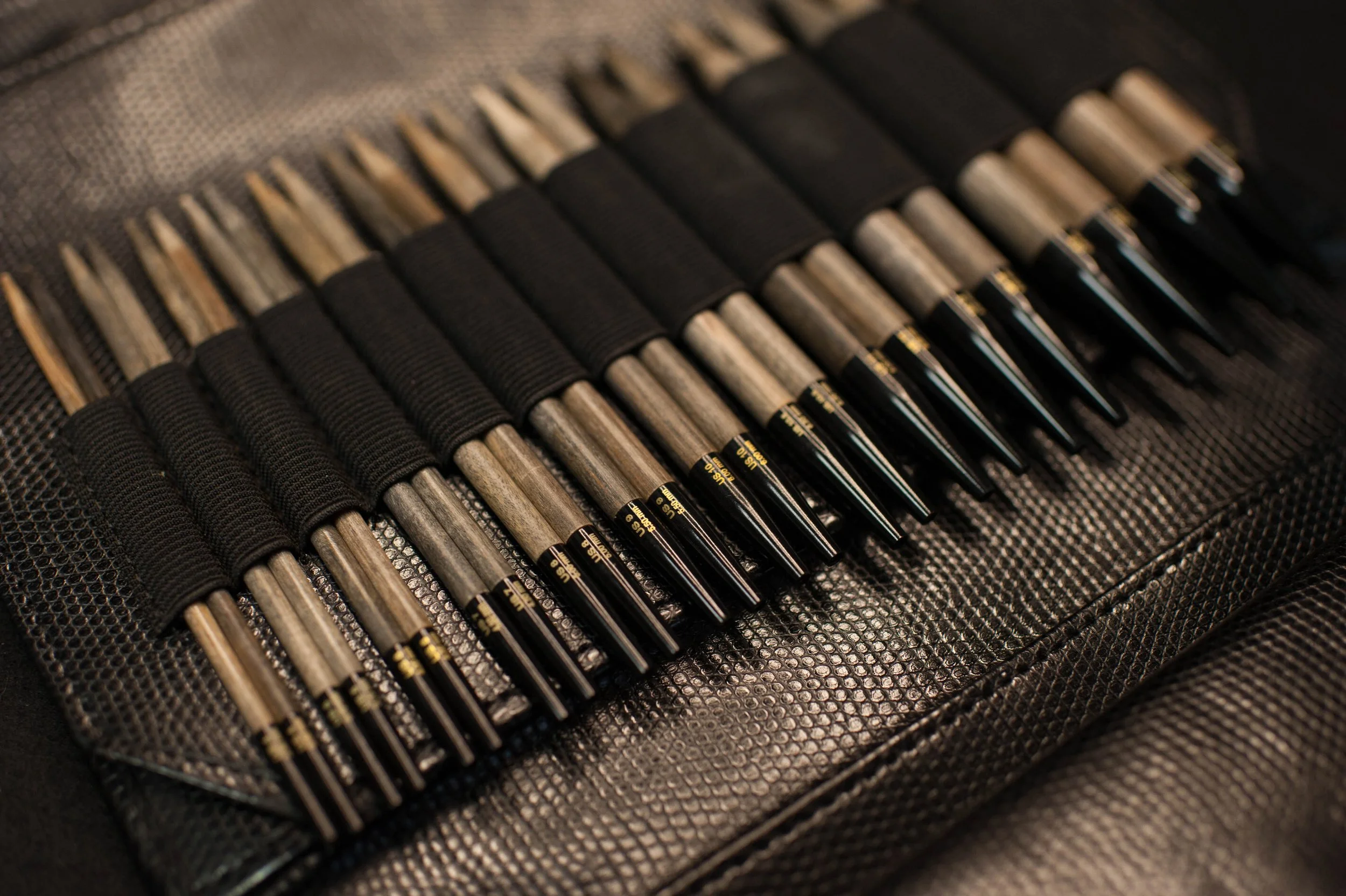 A set of knitting needles, neatly organized in a black carrying case, secured with elastic straps.