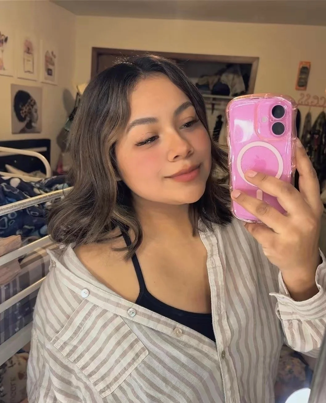A man with dark curly hair, glasses, and a beard, wearing a black sweater, sitting indoors with a neutral background and a plant in the background.