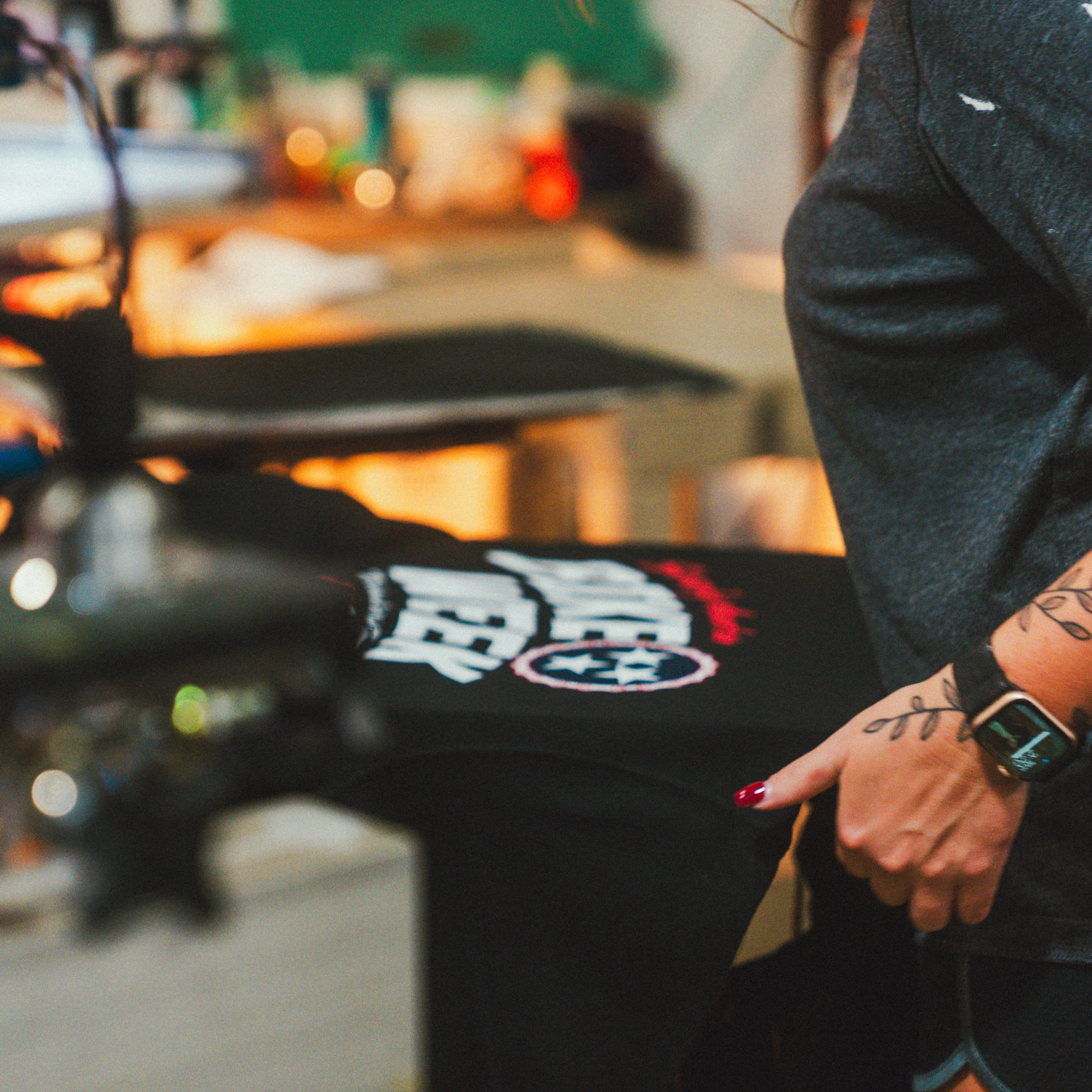 Close-up of a person's hand pointing at a black t-shirt with a logo on it, in an indoor setting.