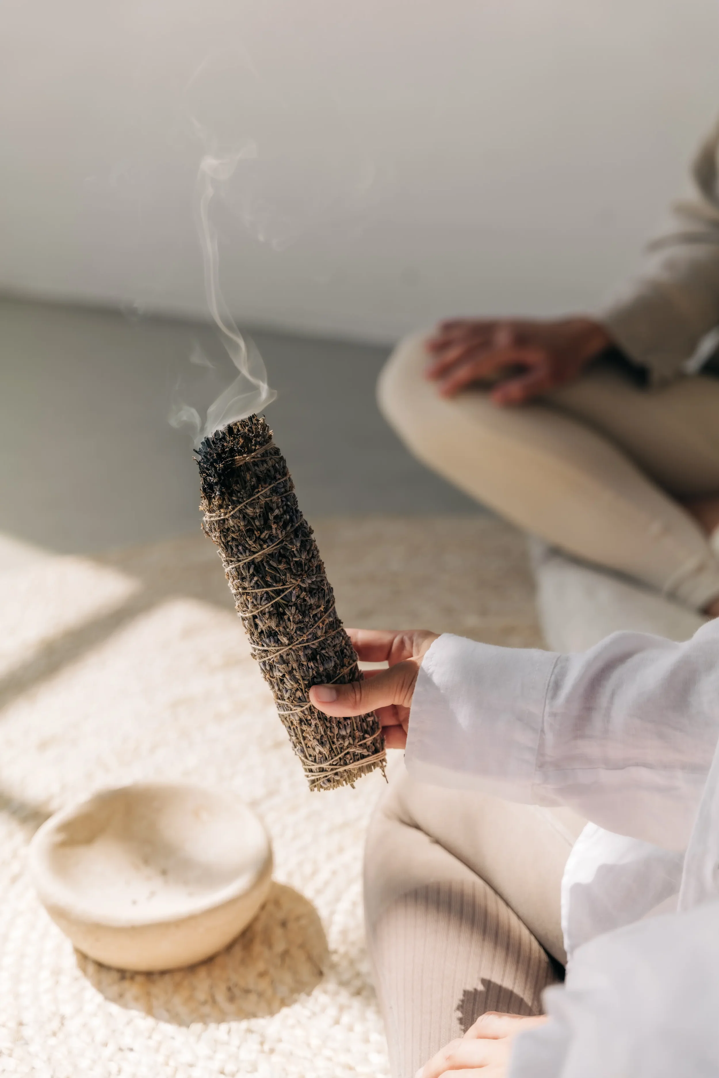 Glimmendes Räucherbündel weißer Salbei in der Hand einer Frau die ein Reinigungsritual mache