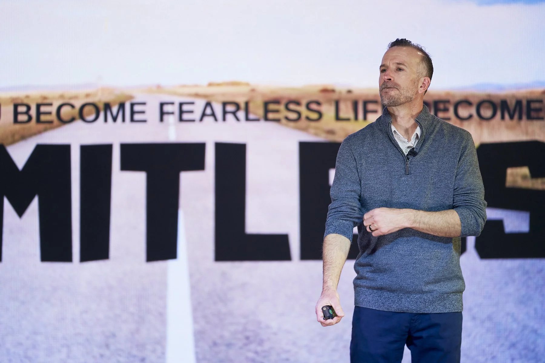 Adam Hill, keynote speaker, standing on a stage with a background of a road and a motivational phrase that says "Limitless."