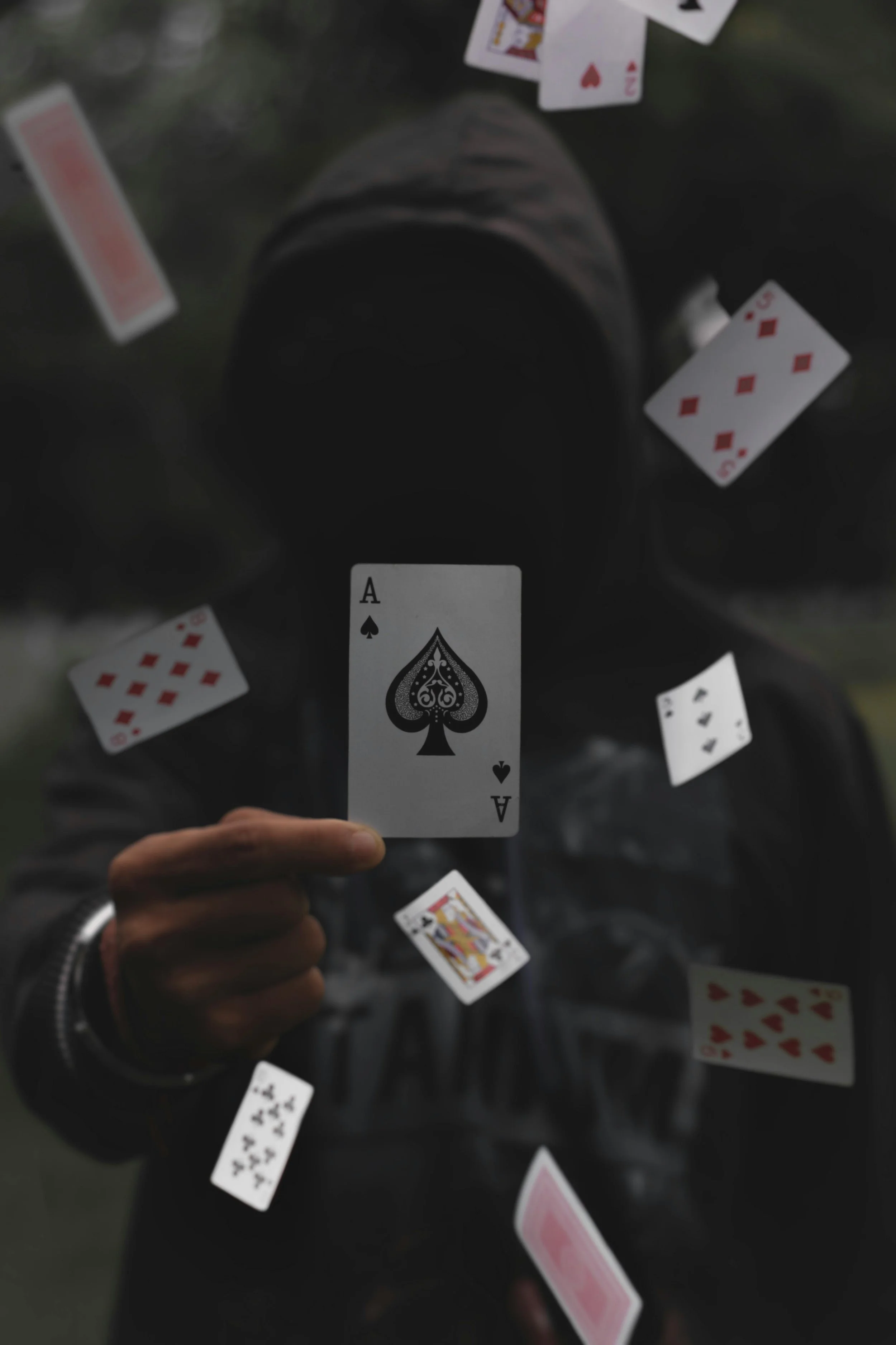 A person holding an ace of spades playing card surrounded by other scattered playing cards.