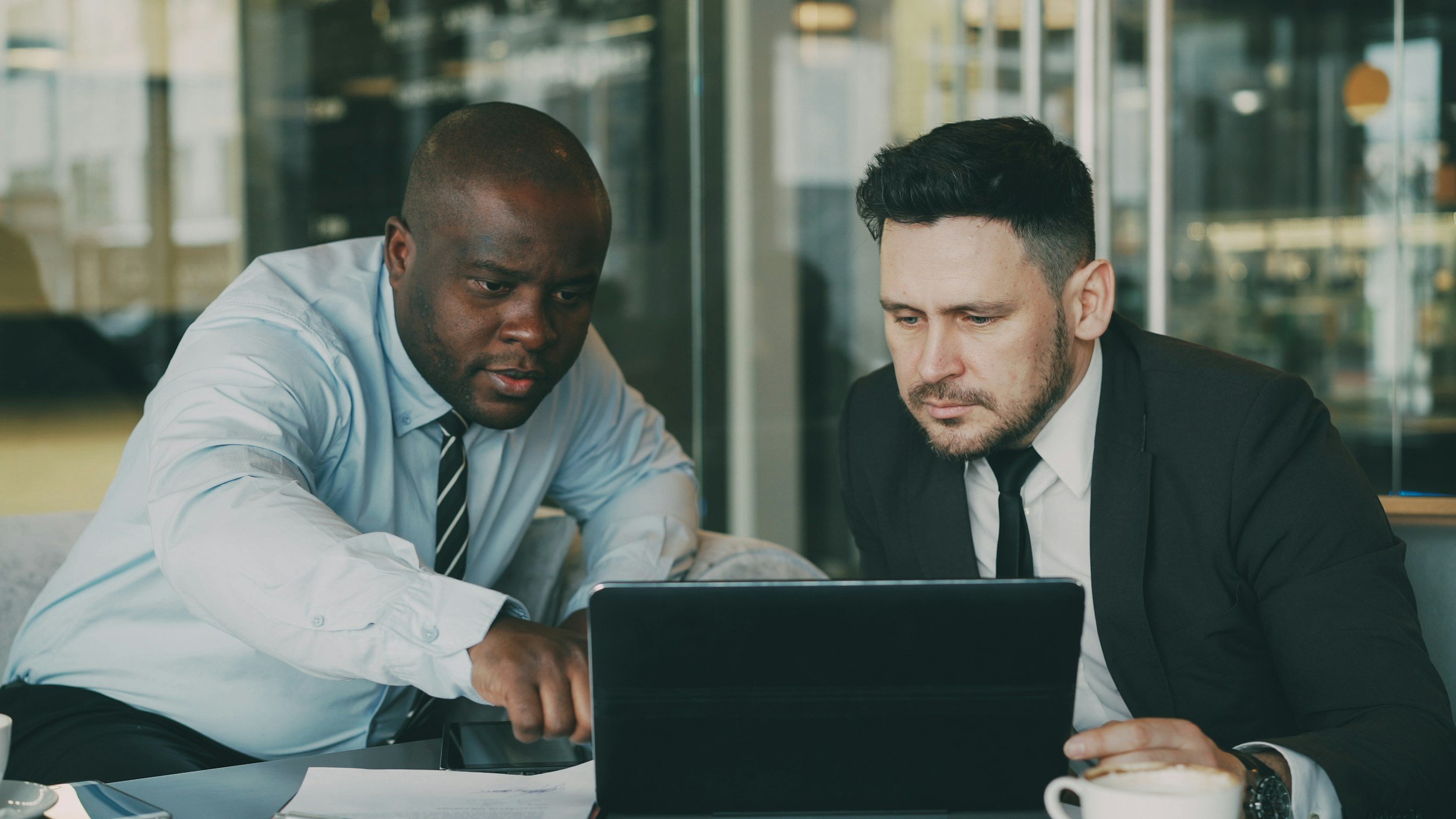 Two businessmen in formal attire working together on a laptop at a modern office desk.