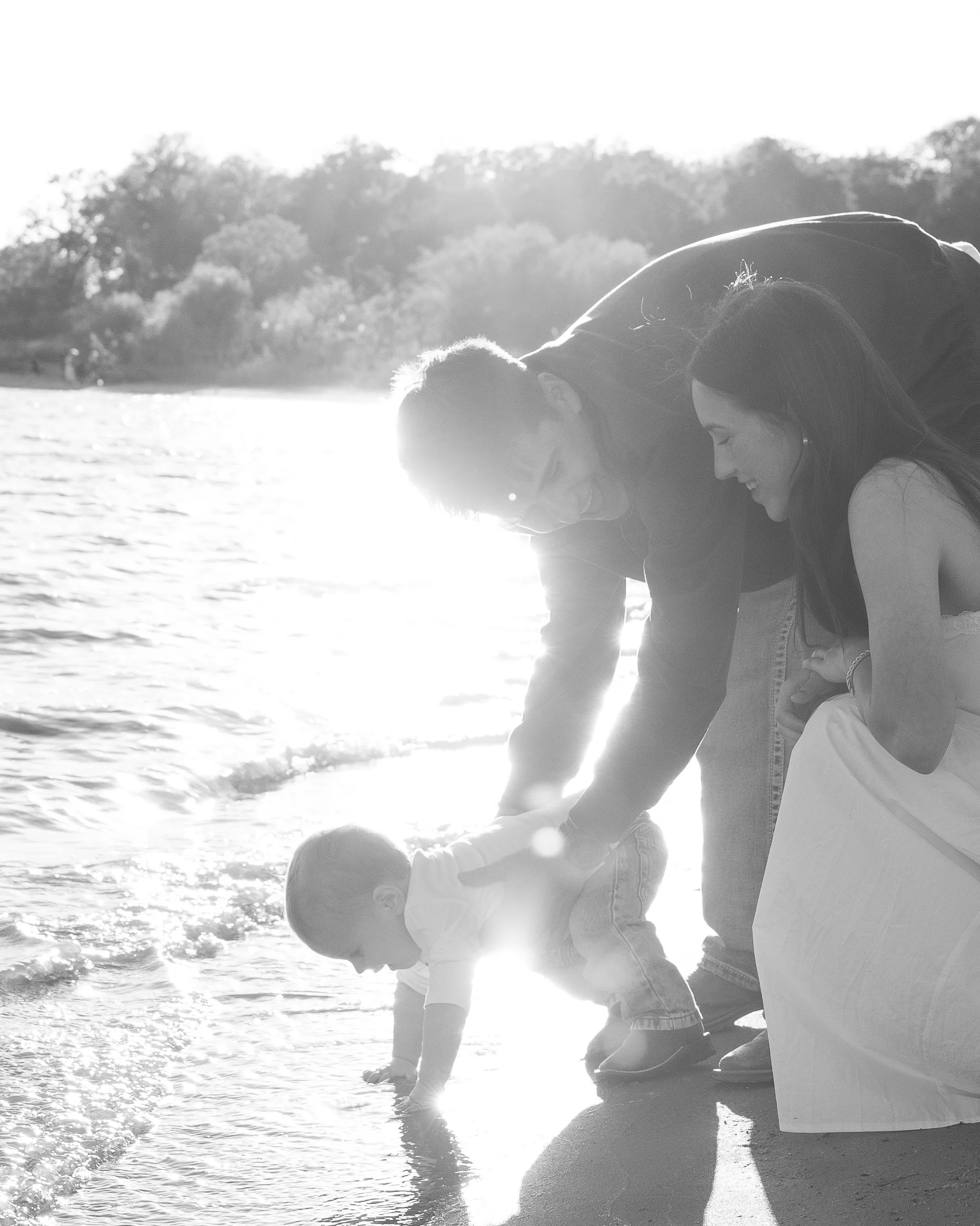 Family playing with a young boy on the beach at sunset, smiling and enjoying the water.
