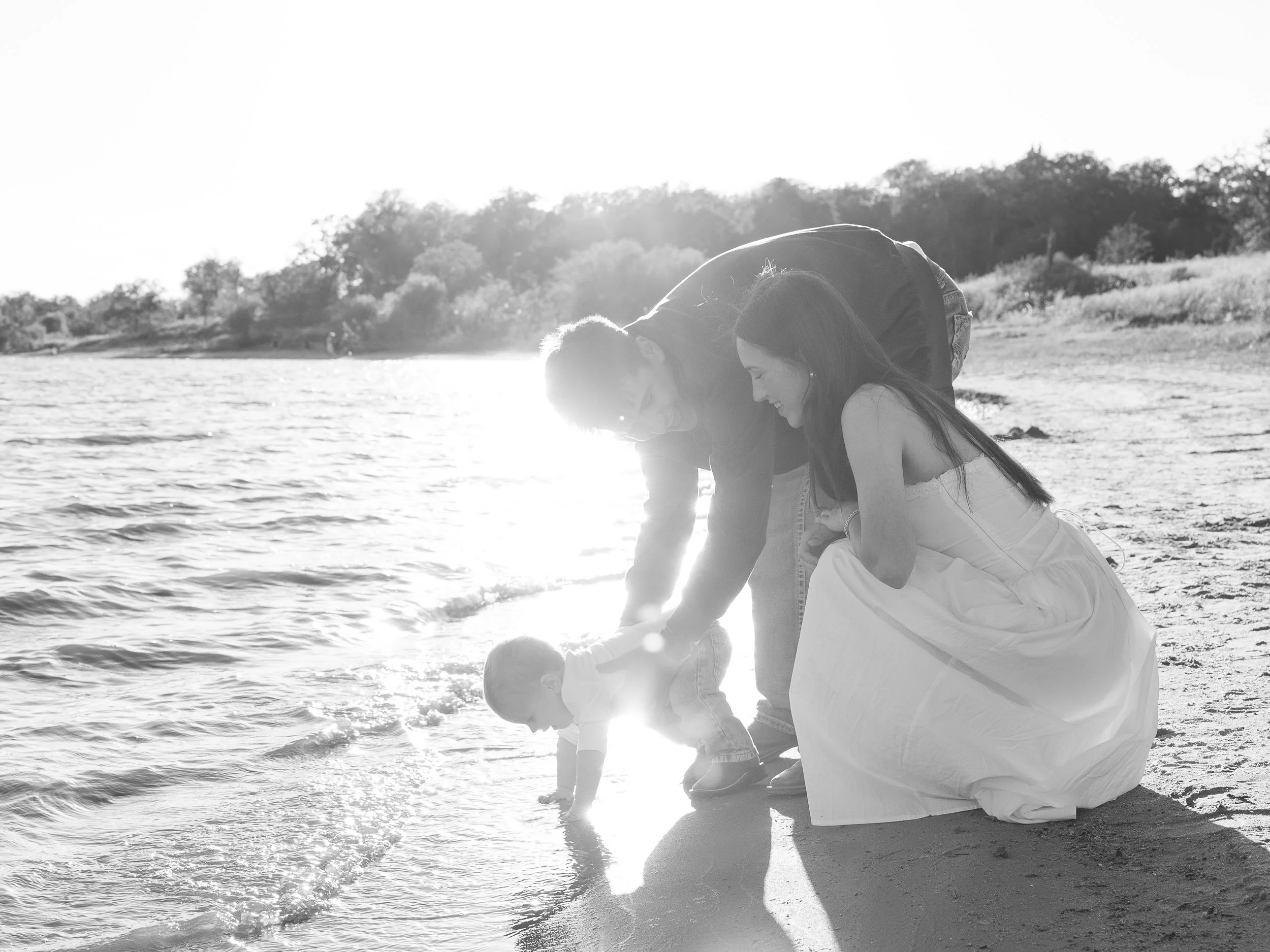Family playing with a baby by the water at the beach during sunset