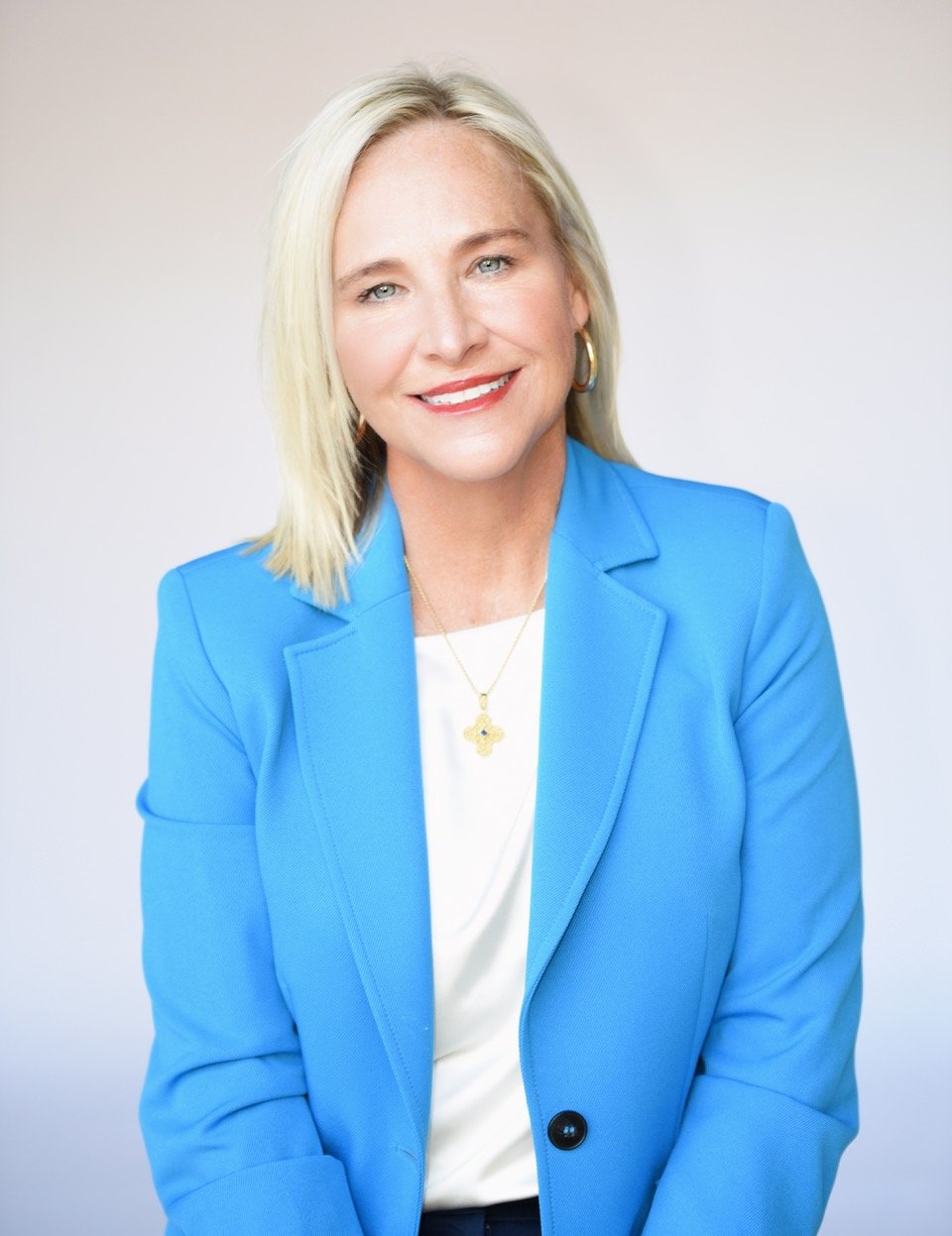 Portrait of claire, LPC, therapist in Lafayette, Louisiana with blonde hair wearing a blue blazer, white top, and gold jewelry, smiling at the camera.