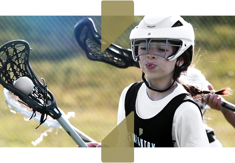 Youth lacrosse player wearing a helmet and holding a lacrosse stick during a game.