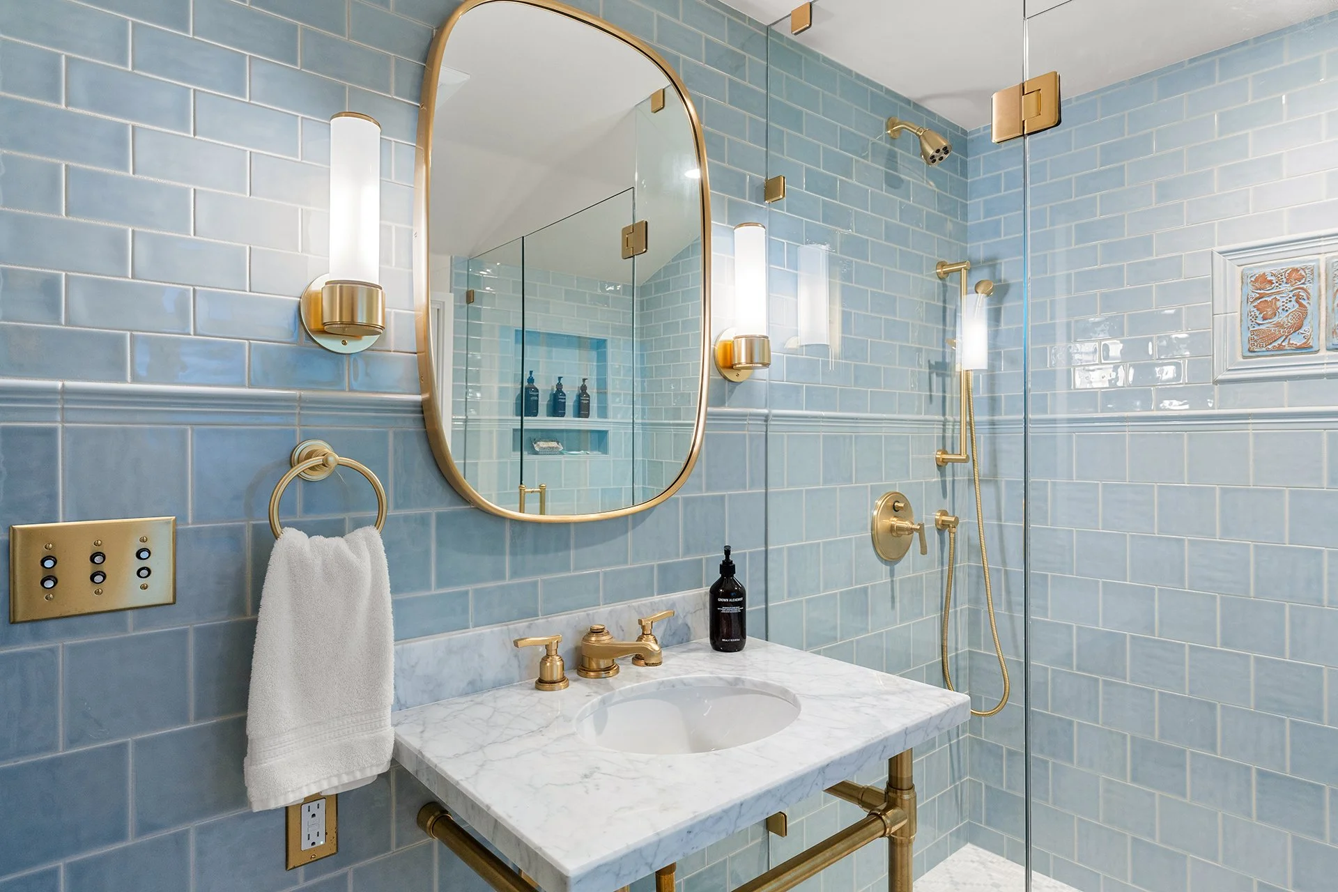 Luxury bathroom remodel with blue tile walls, marble countertop vanity, and brushed gold fixtures, featuring a glass enclosed shower designed for high end residential construction.
