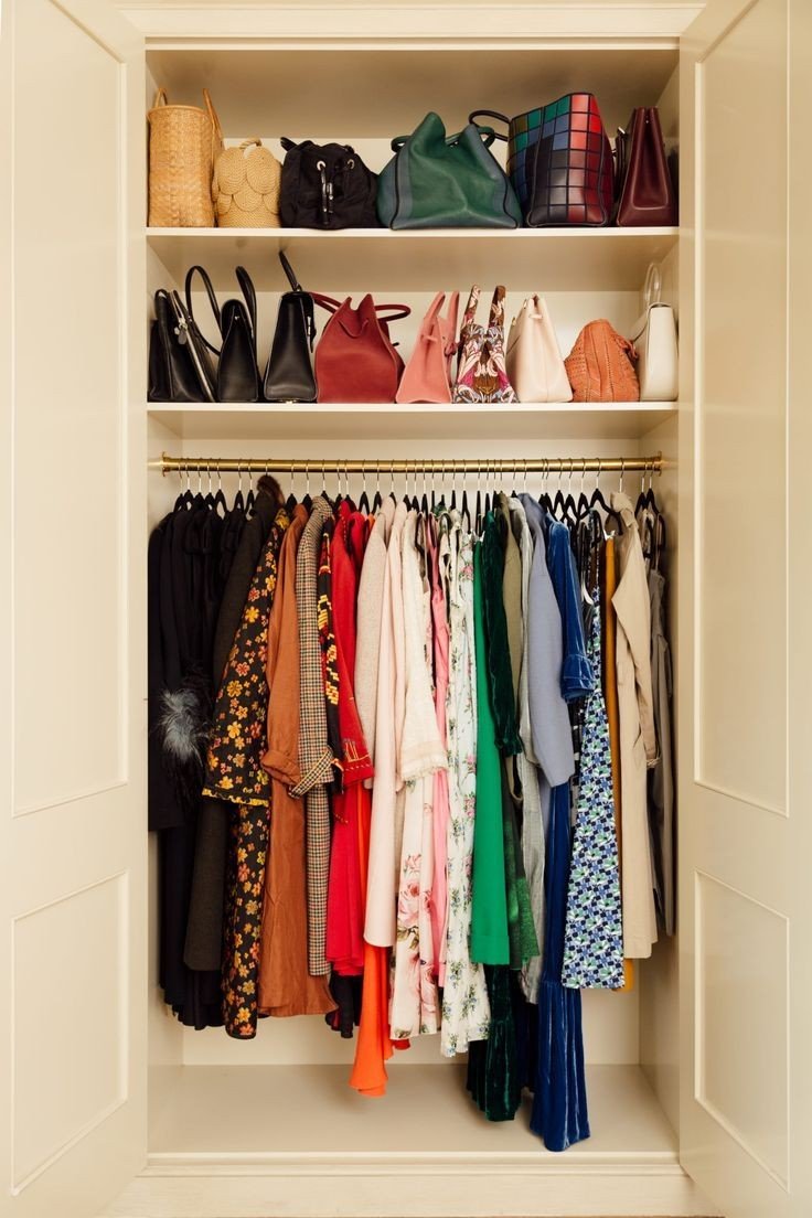 Inside an organized wardrobe with hanging dresses and blouses below, and shelves of handbags and accessories above.
