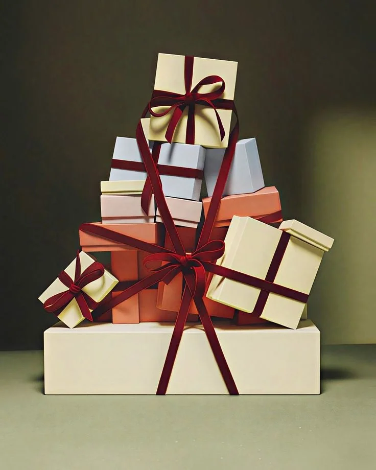 A wrapped gift box with floral patterned paper, tied with a wide green satin ribbon and decorated with a small gold ornament.