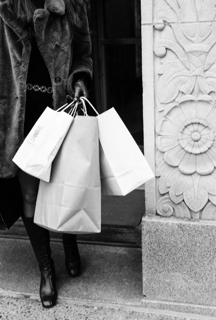 Woman in a fur coat holding shopping bags outside a building with decorative stone carvings.