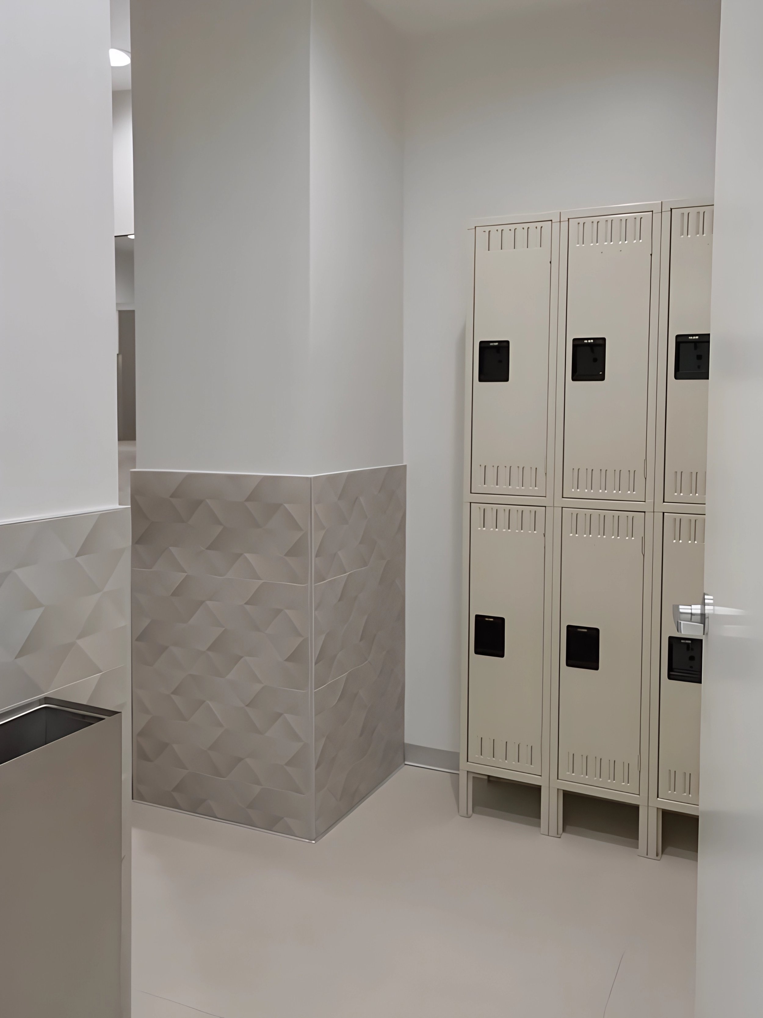 Set of beige lockers with black locks in a room with white walls and geometric-patterned tiled half-wall.