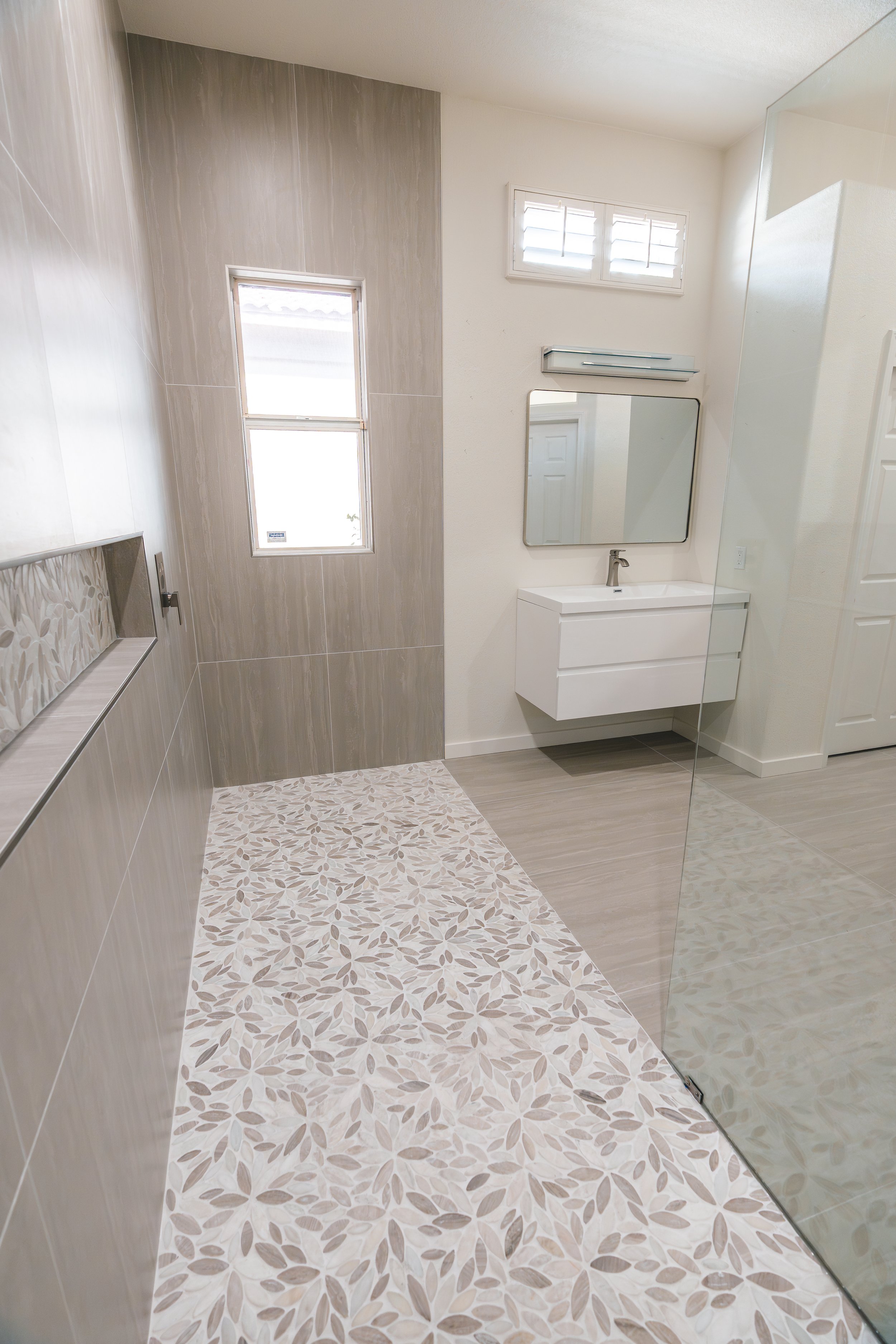 Modern bathroom with a glass shower, wall-mounted vanity, and neutral-colored floor and wall tiles.