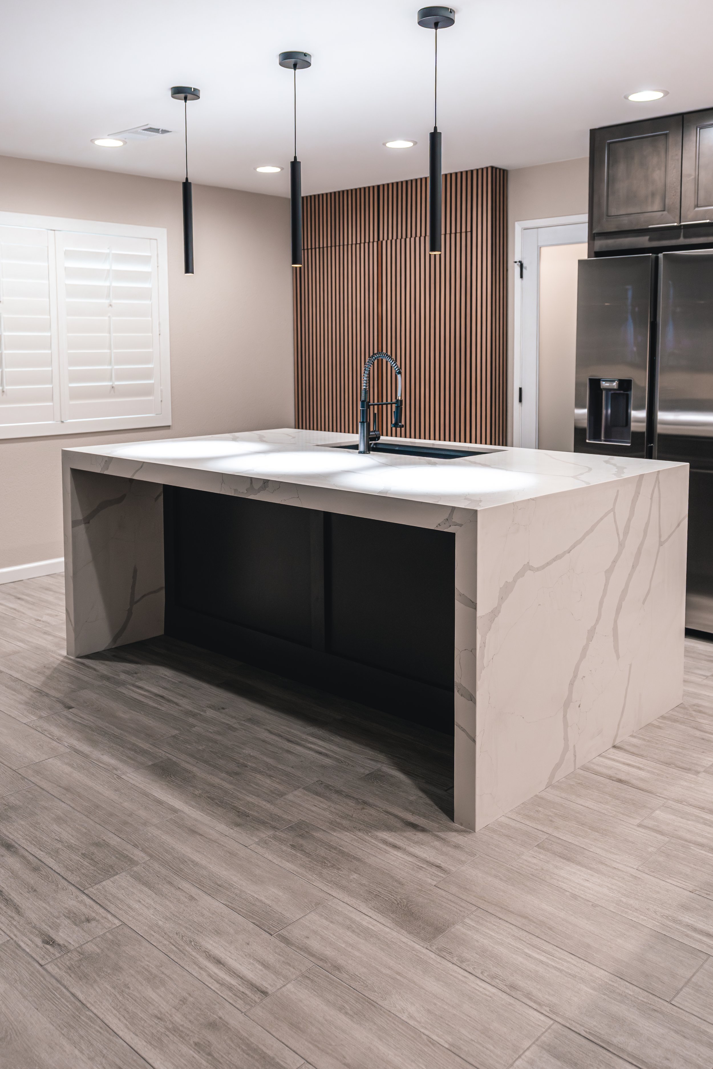 Modern kitchen with a white marble island, black faucet, and pendant lighting fixtures.