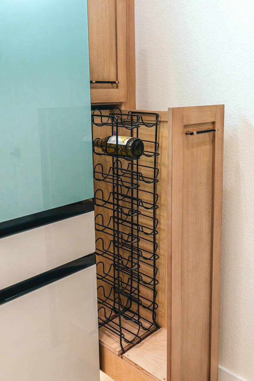 Kitchen corner with wooden cabinets, a wine rack with bottles, and a small fridge.