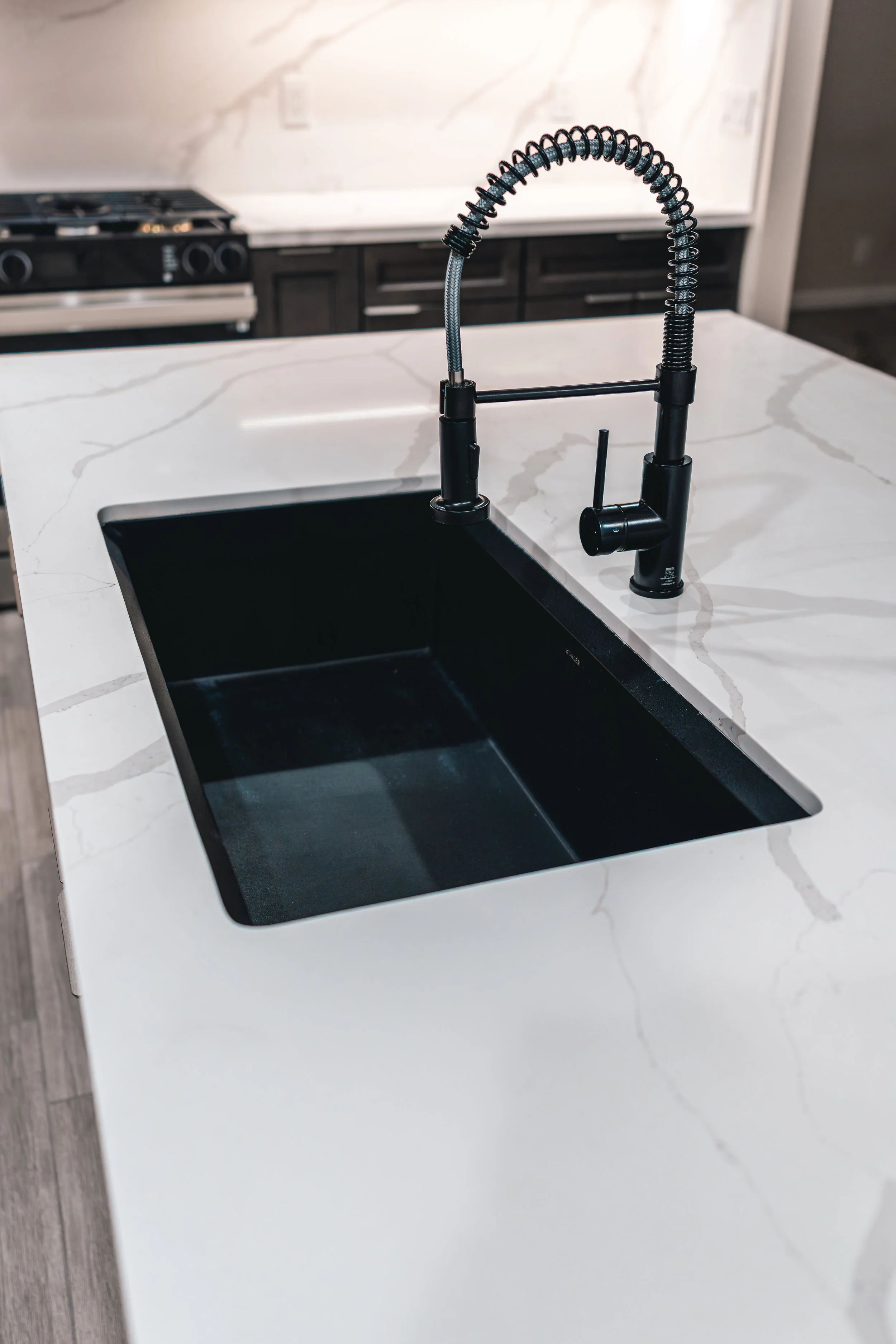 Kitchen sink with black basin and modern black faucet on white marble countertop.