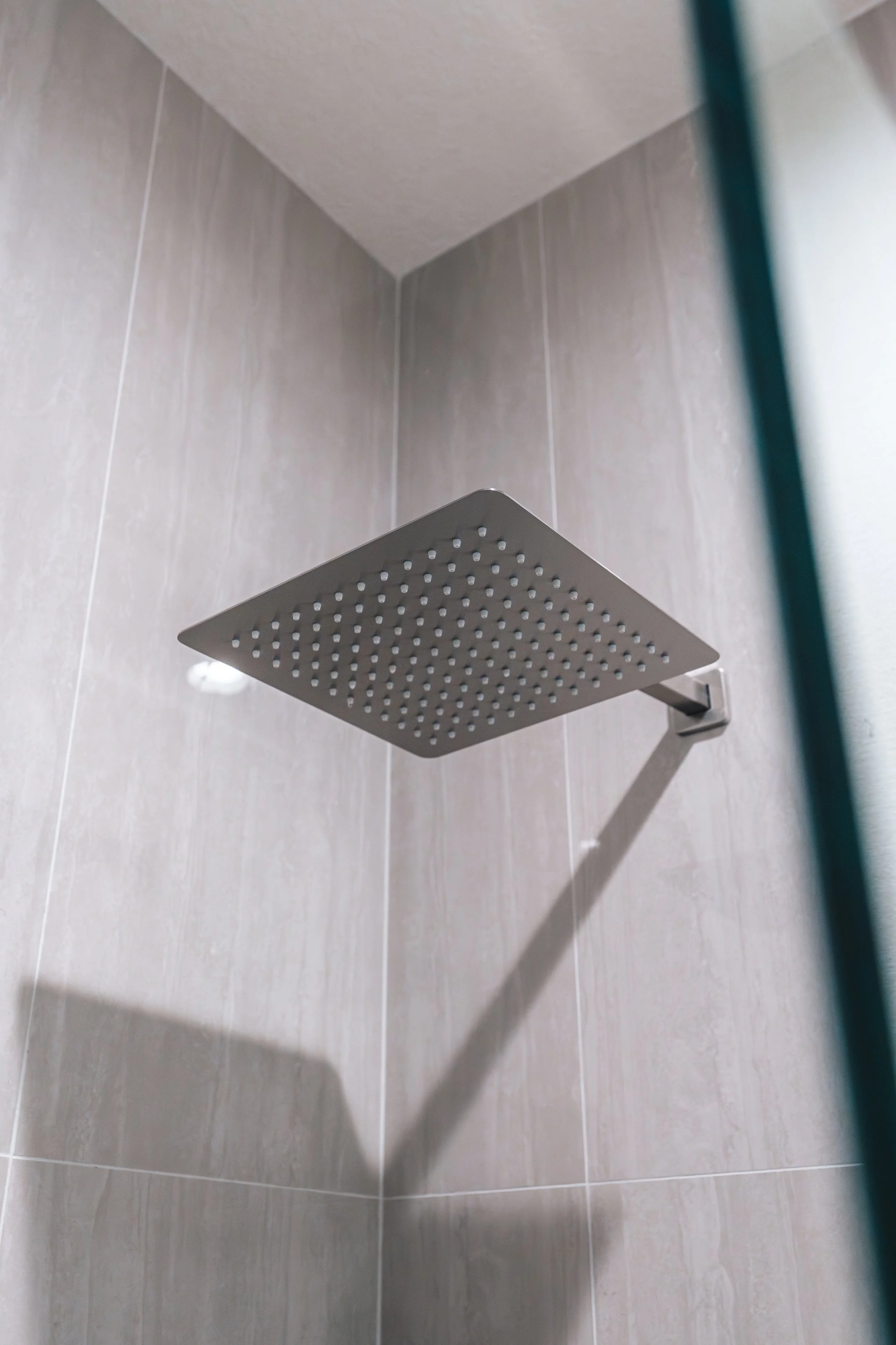 Close-up of a modern square showerhead mounted on a tiled shower wall.